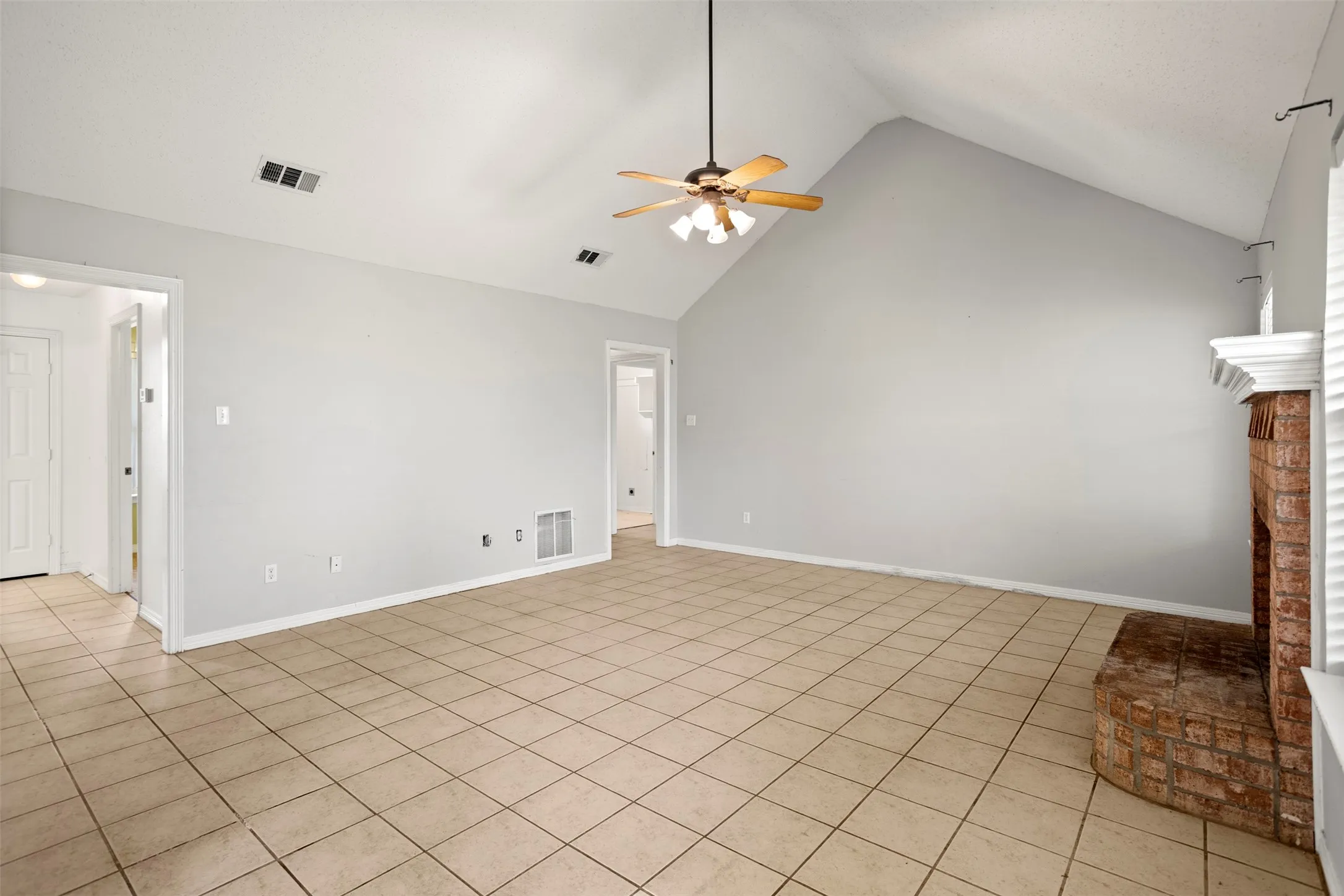 Unfurnished living room featuring a high ceiling, a ceiling fan, light tile patterned flooring, and a brick fireplace