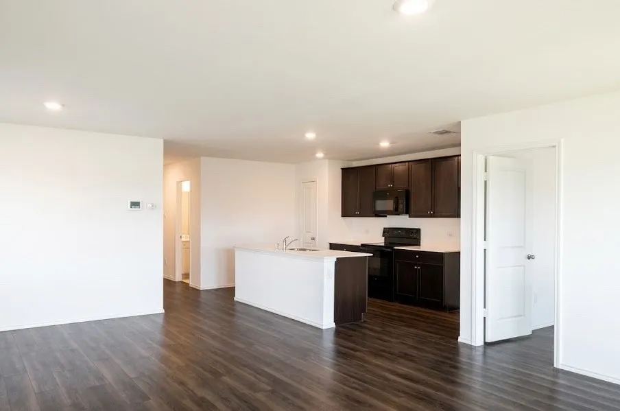 Kitchen featuring light countertops, dark wood finish cabinets, black appliances, an island with sink, and dark wood finished floors
