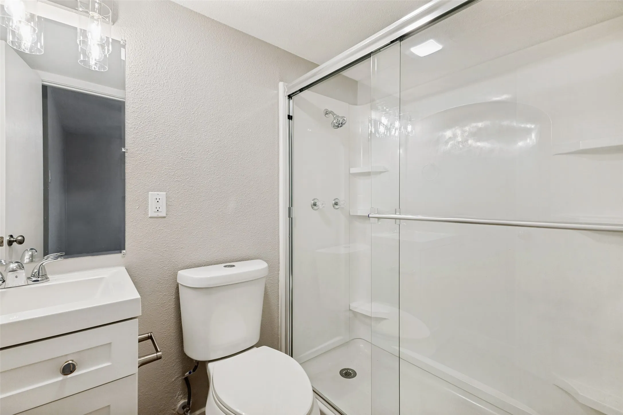 Bathroom with a textured wall, vanity, and a stall shower