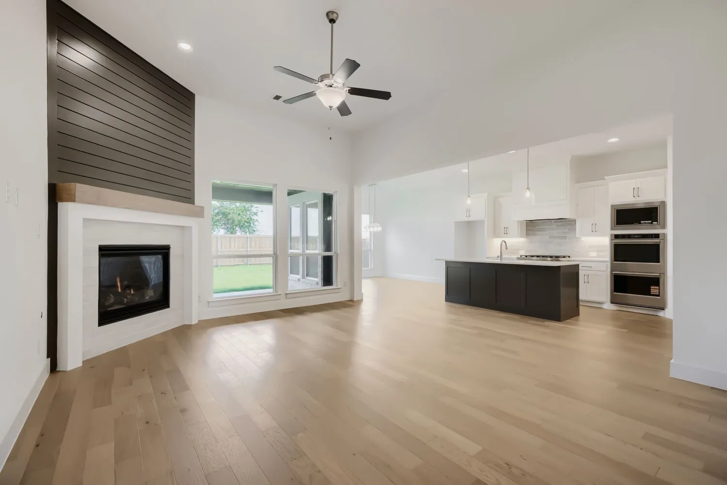 Spacious living area featuring light wood-finish flooring and a vaulted ceiling with a ceiling fan