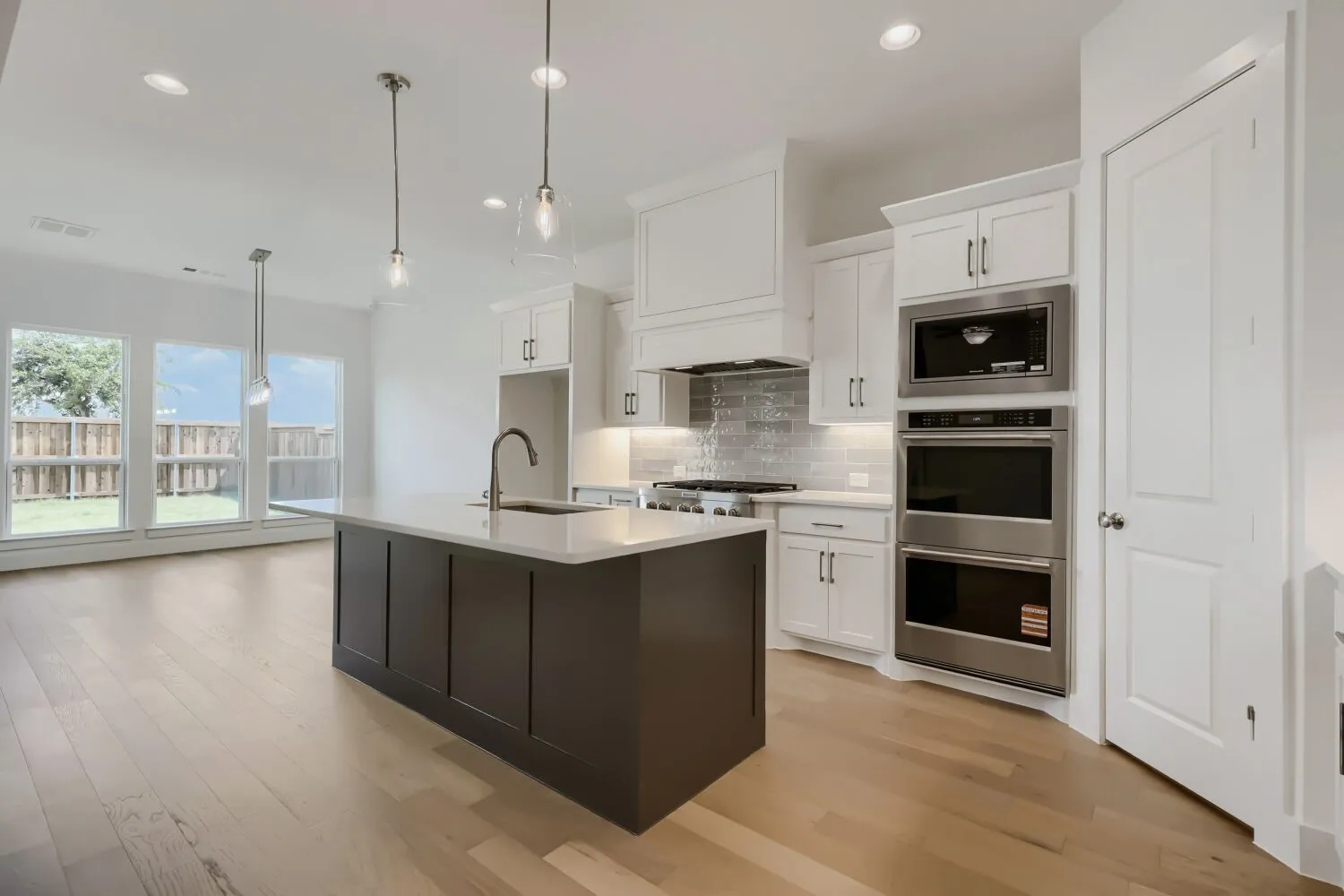 Modern kitchen featuring a dark-toned island with an undermount sink, pendant lighting, light wood-finish flooring, white cabinetry, and stainless steel appliances