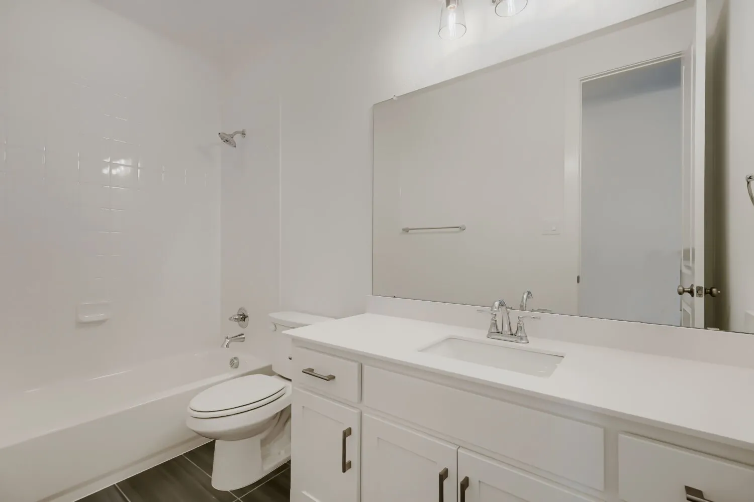 White bathroom featuring a built-in tub with a tiled surround, a white vanity with an undermount sink, a large wall-mounted mirror, and wood-finish flooring