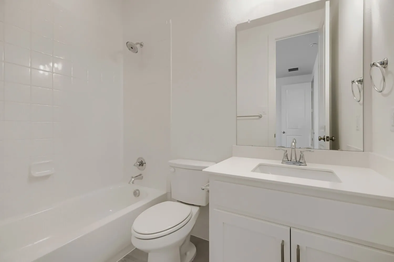 Bathroom featuring a white bathtub with subway tile surround, polished chrome fixtures, a white vanity with an integrated sink, and a large wall-mounted mirror
