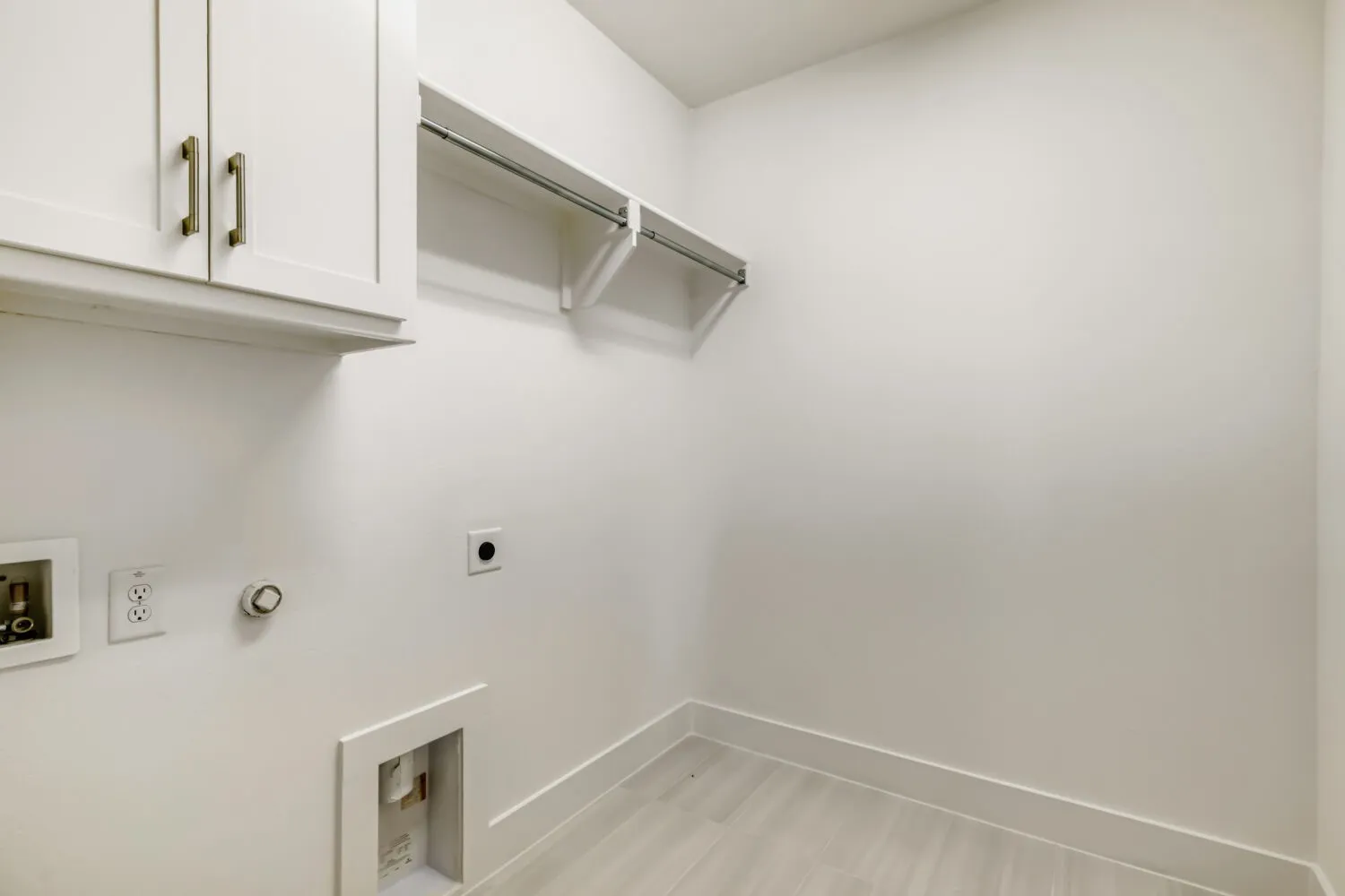 Bright utility space featuring white upper cabinetry with bronze hardware, a built-in hanging rod, and light wood-finish flooring
