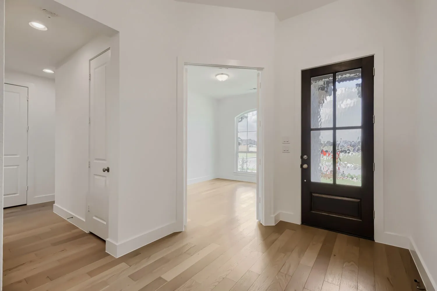 Entryway featuring a dark wood-finish door with textured glass panels, light wood-finish flooring, recessed lighting, and crisp white walls