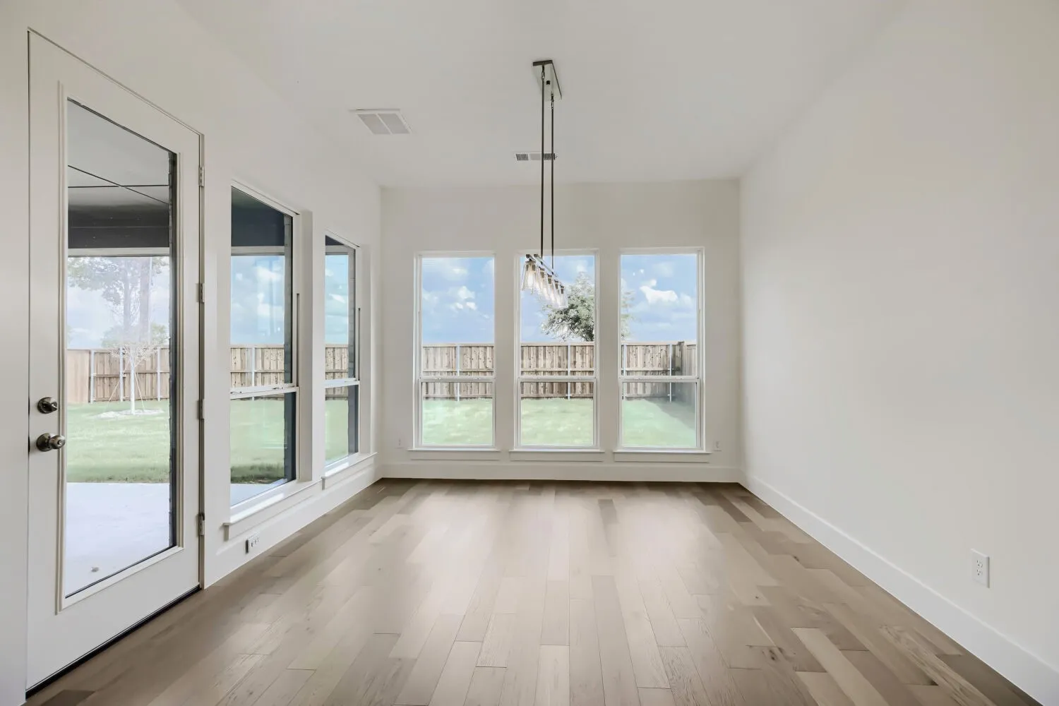 Spacious interior with wood-finish flooring, white walls, and a modern linear pendant light fixture