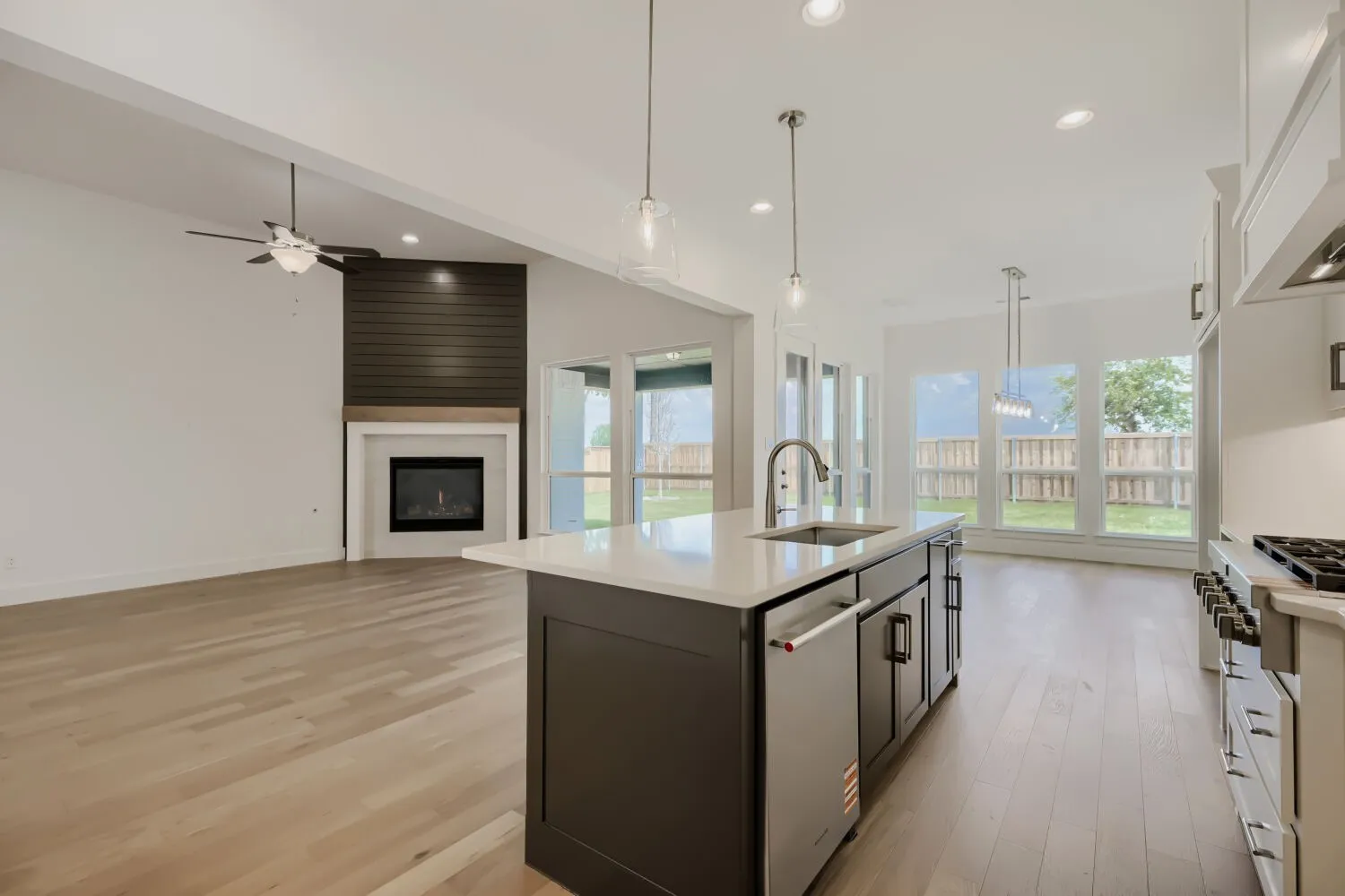 Open-concept living space featuring wood-finish flooring, a contemporary fireplace with shiplap accent wall, and a kitchen island with sink and pendant lighting