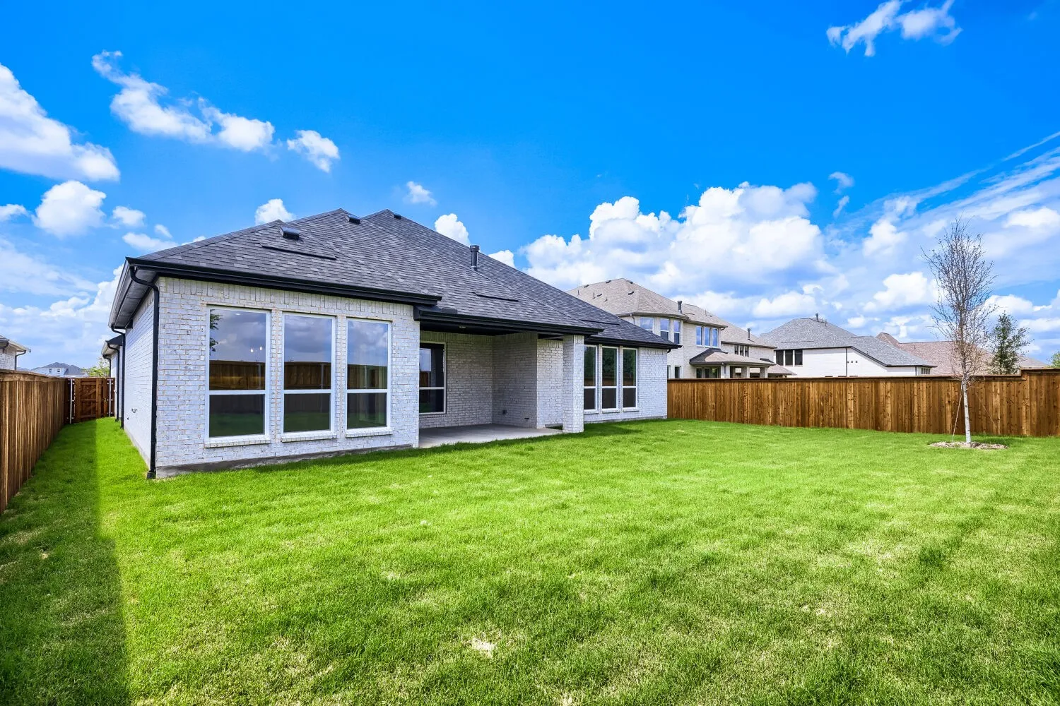 Expansive backyard featuring a manicured lawn, full privacy fencing, and a mature tree