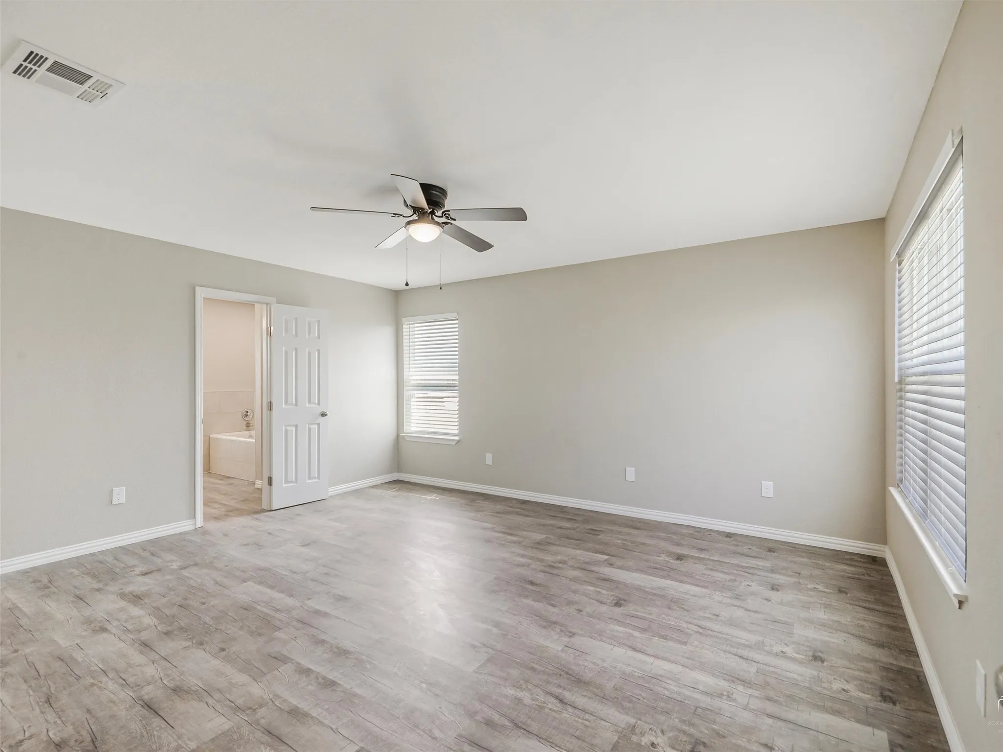 Spacious bedroom featuring wood-finish flooring, a ceiling fan with integrated lighting, and a window with blinds