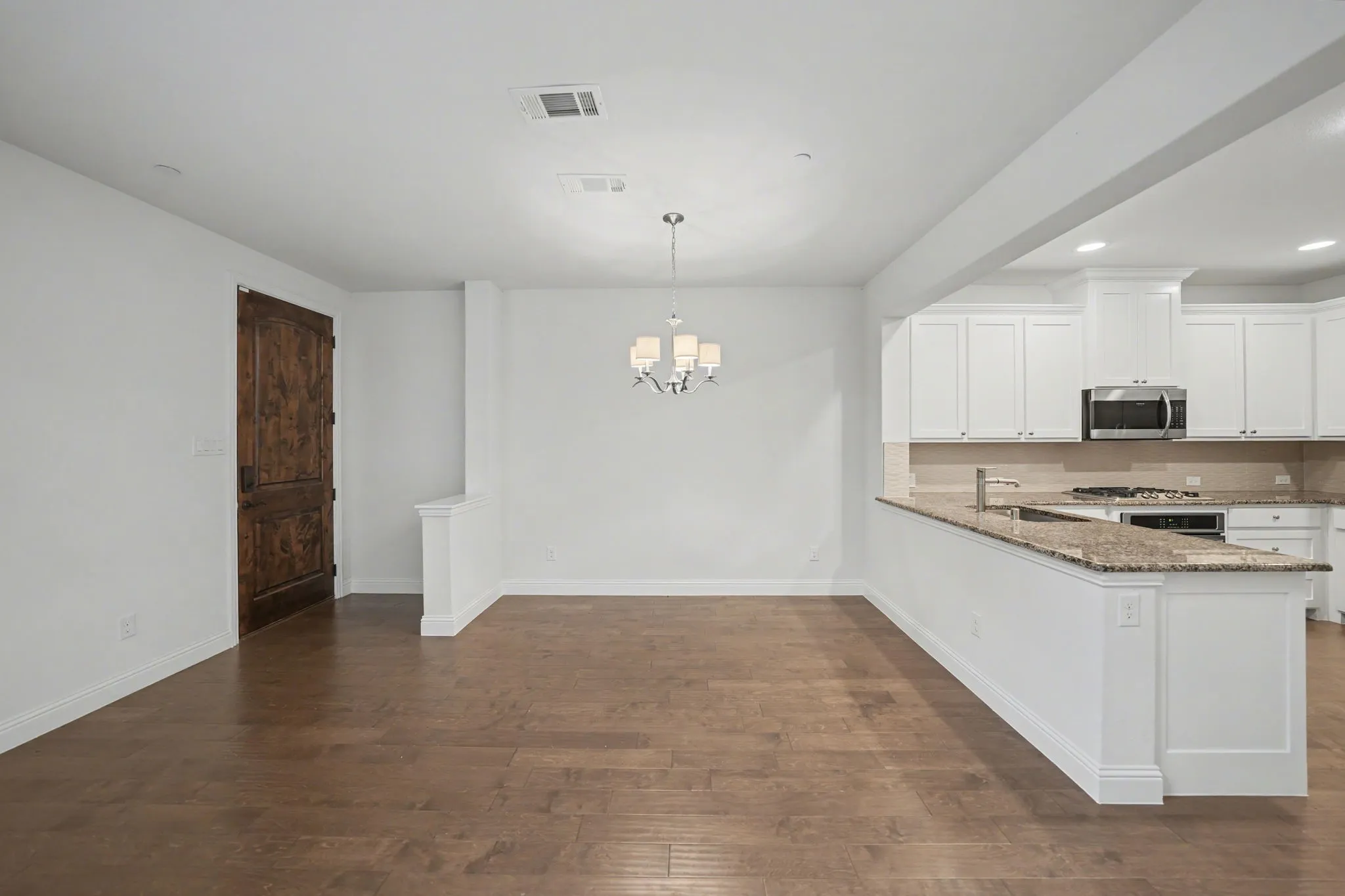 Kitchen with light stone counters, white cabinetry, dark wood flooring, a peninsula, and suspended lighting
