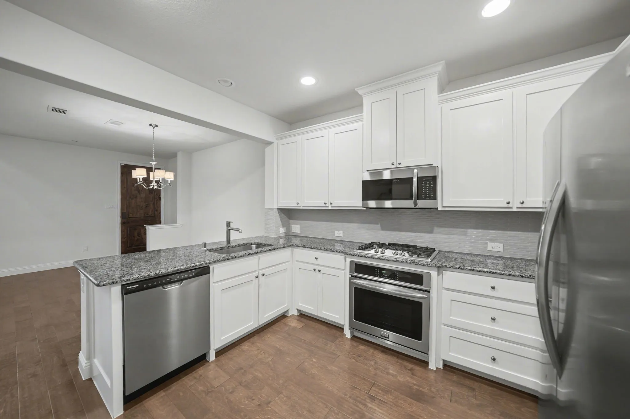 Kitchen with stainless steel appliances, light stone countertops, a peninsula, and white cabinets