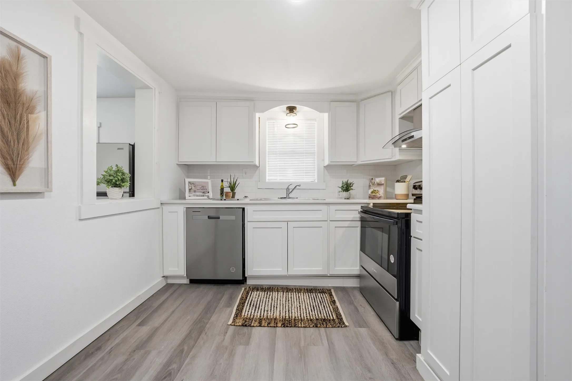 Kitchen featuring white cabinets, light countertops, stainless steel appliances, light wood-style flooring, and tasteful backsplash