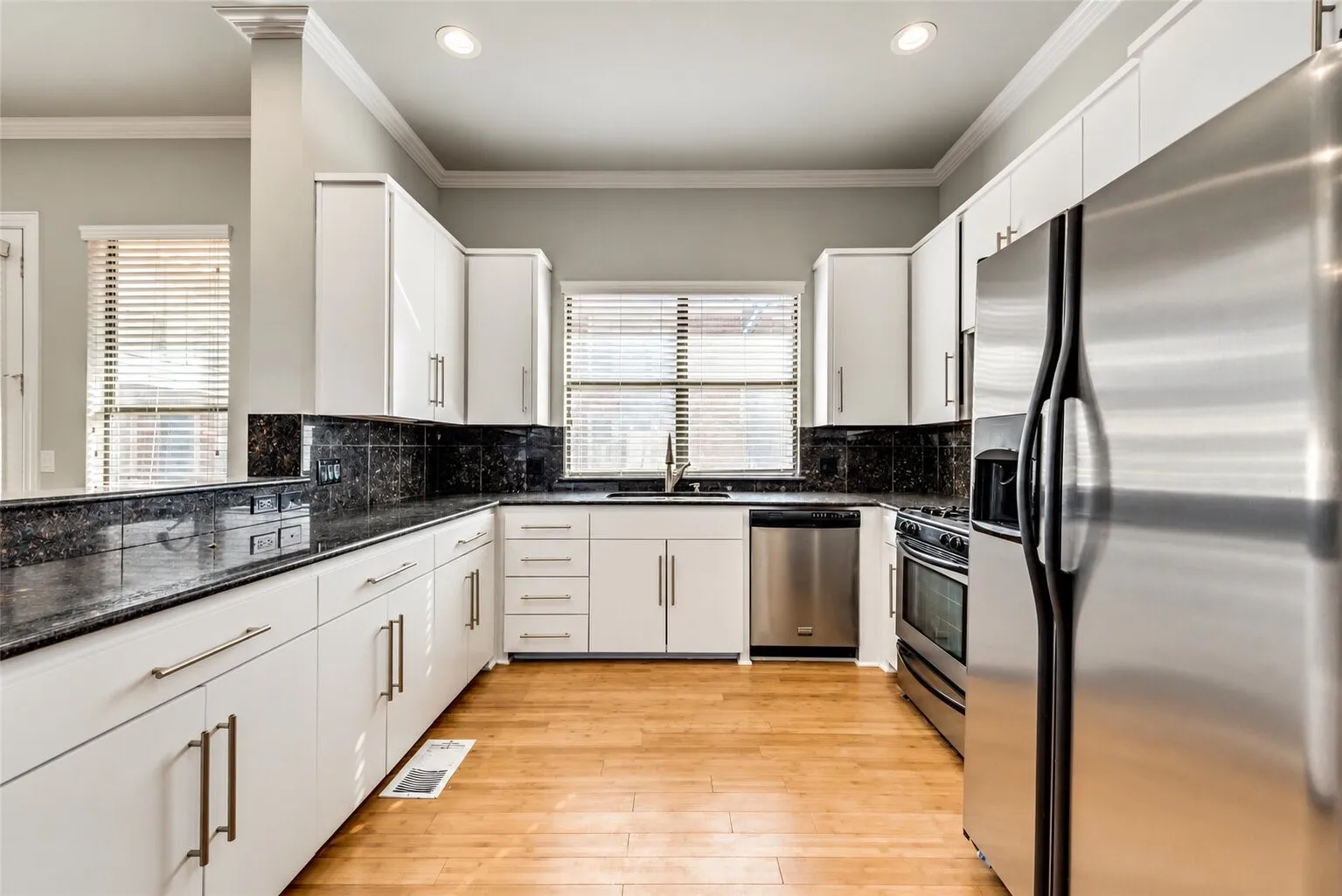 Modern kitchen featuring white cabinetry, dark stone countertops, stainless steel appliances, and wood-finish flooring