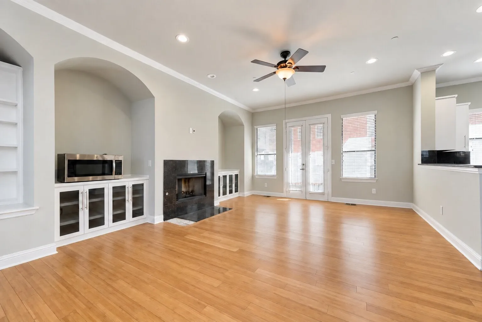 Hardwood-finish flooring, built-in shelving, fireplace with dark stone surround, recessed lighting, and ceiling fan