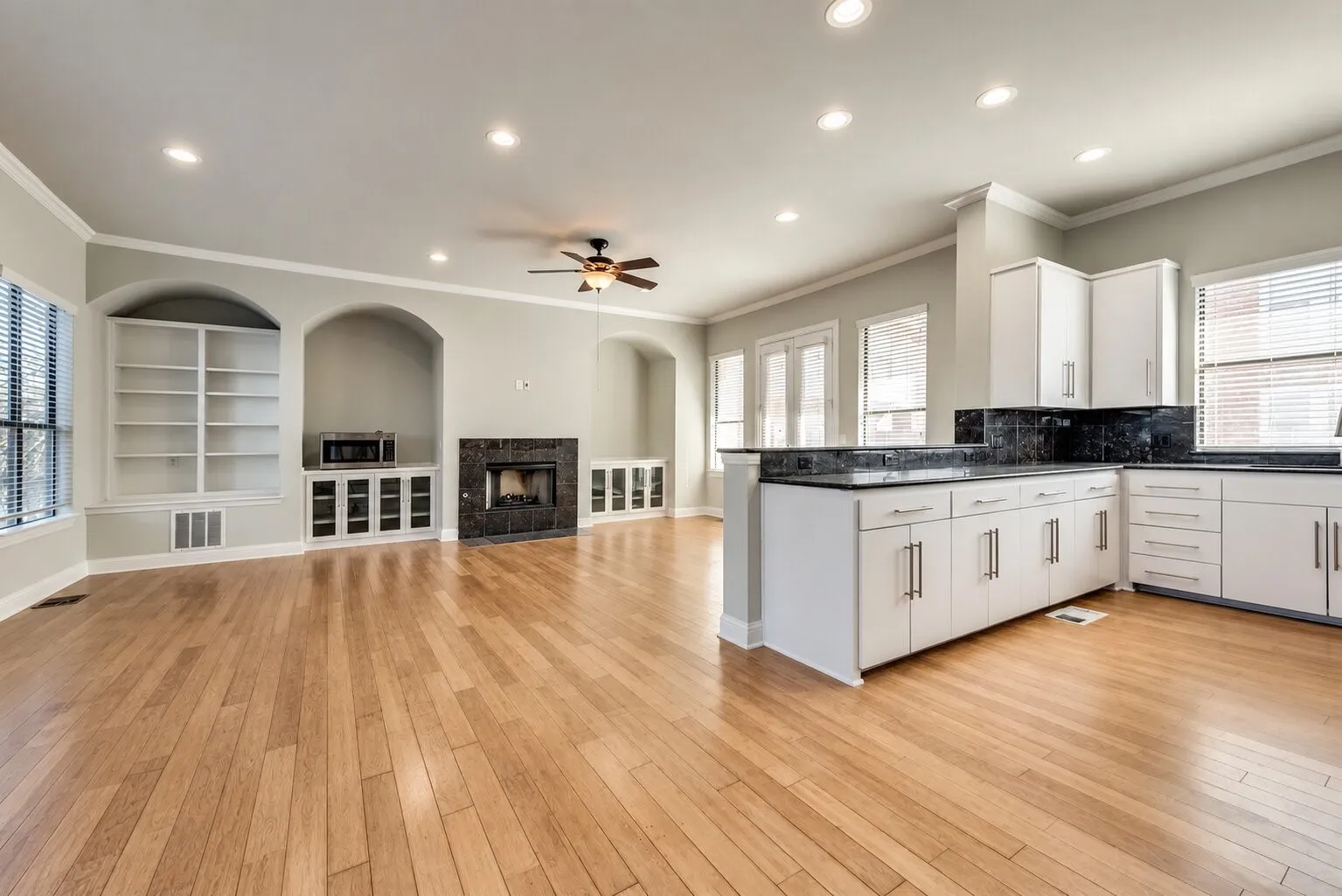 Hardwood flooring throughout, recessed lighting, built-in shelving, stone fireplace surround, and white cabinetry with dark countertops