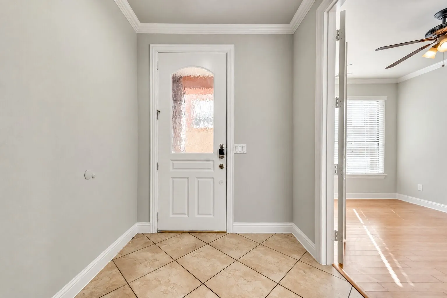Entryway featuring ceramic tile flooring, a white paneled door with decorative glass, crown molding, and light-colored walls