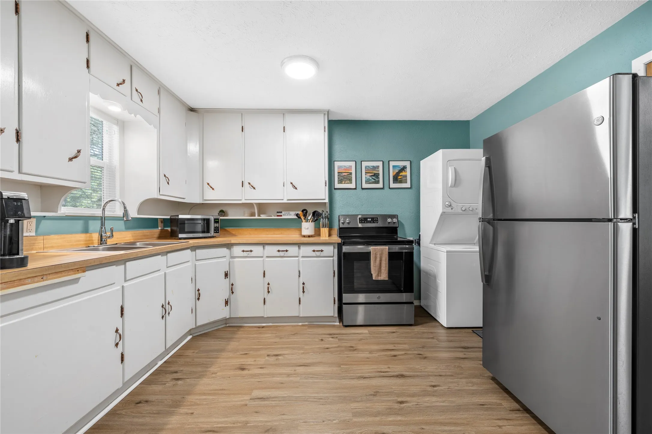Kitchen featuring stainless steel appliances, light wood-style flooring, white cabinetry, and stacked washer and clothes dryer
