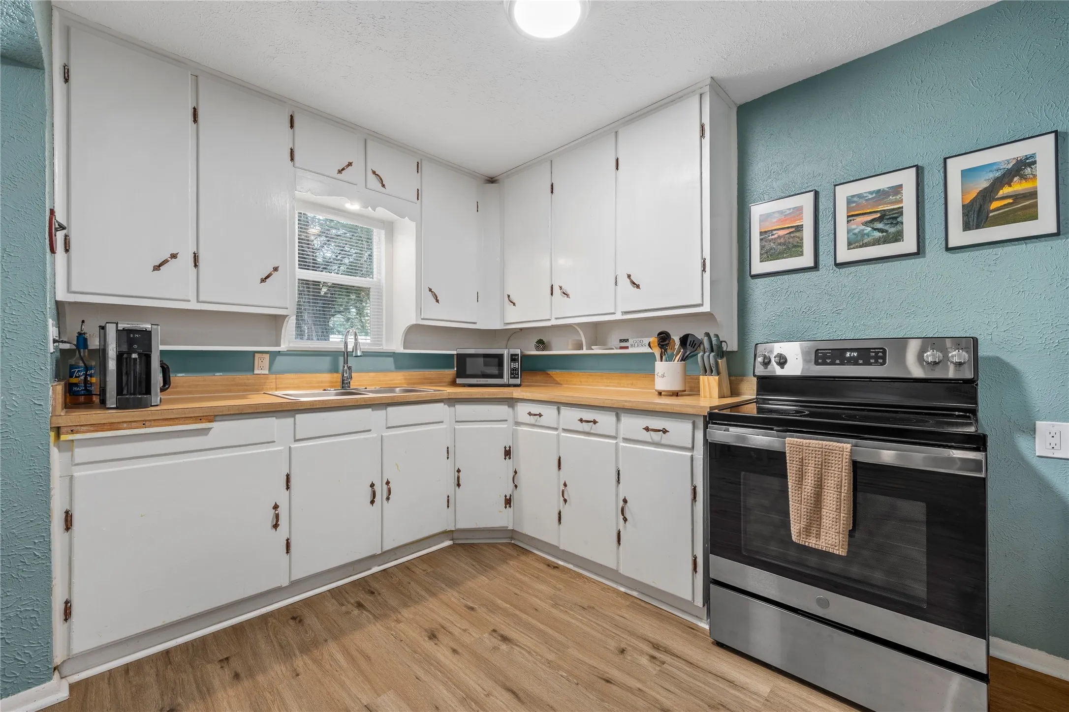 Kitchen with a textured wall, stainless steel appliances, white cabinets, light wood-type flooring, and a textured ceiling