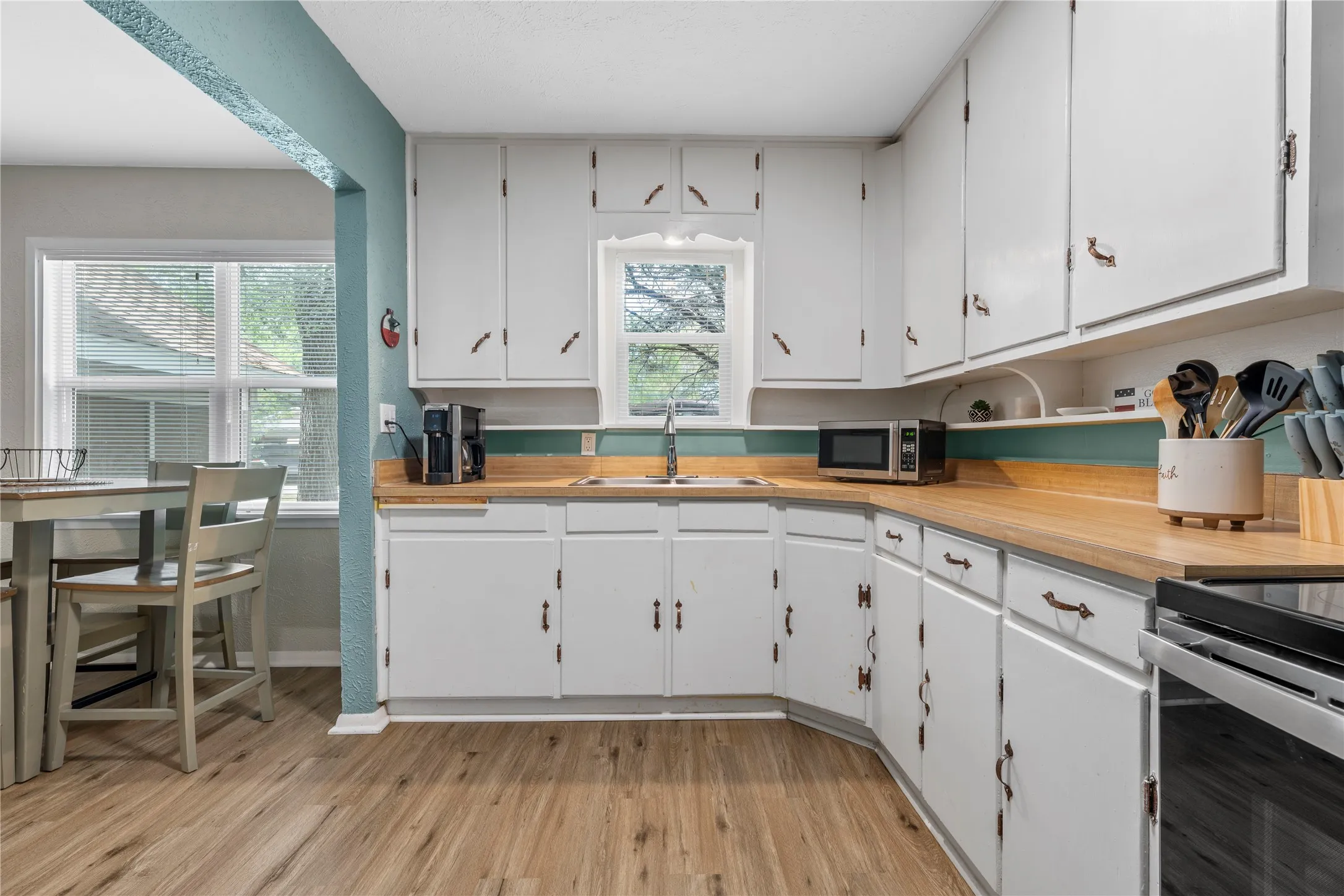 Kitchen featuring light wood-type flooring, stainless steel appliances, white cabinetry, and wooden counters