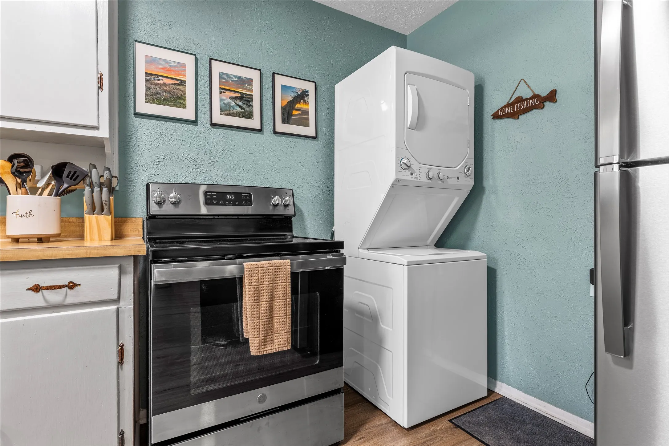 Kitchen with a textured wall, stainless steel appliances, white cabinets, light wood finished floors, and stacked washer / drying machine