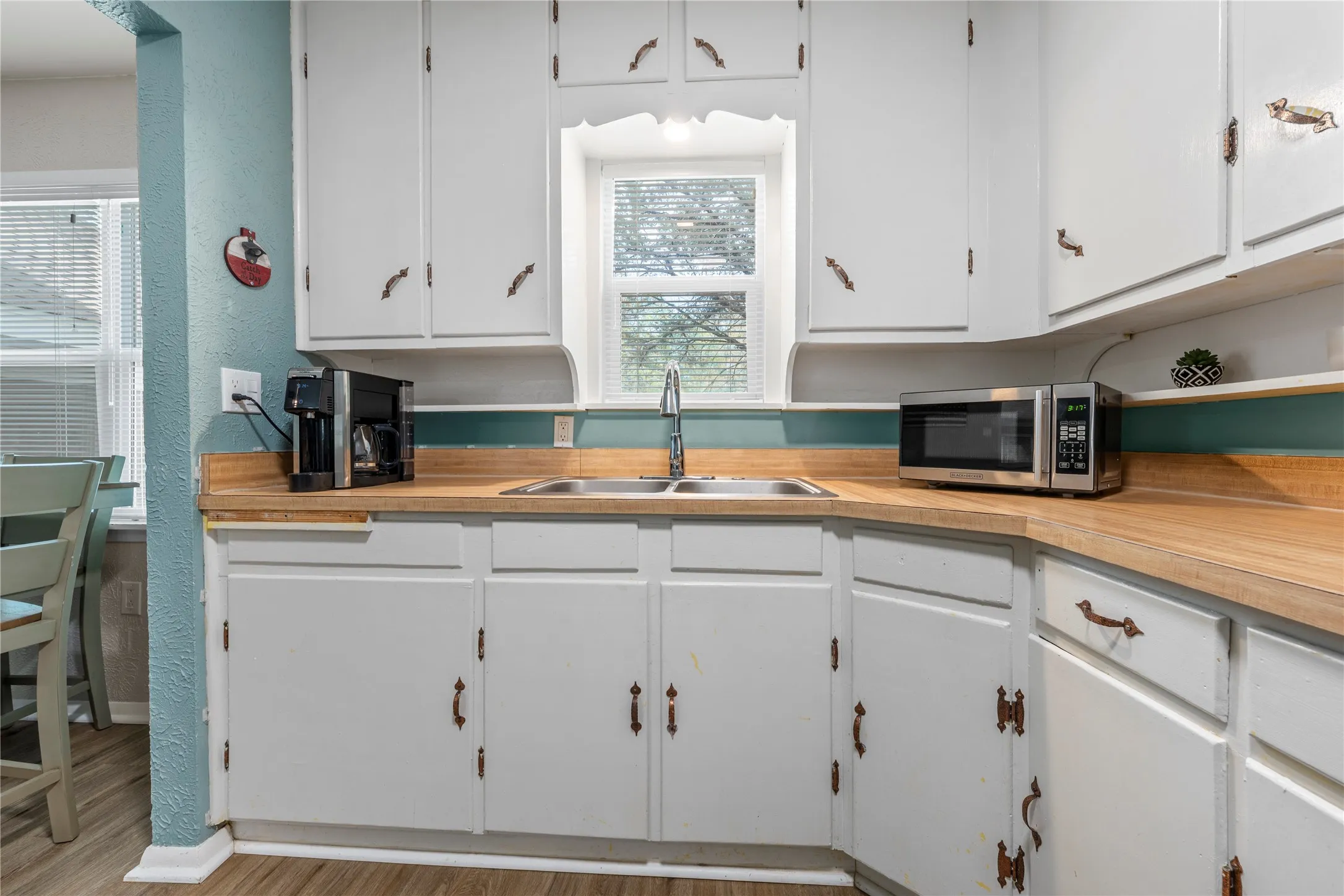 Kitchen with white cabinets, light countertops, stainless steel microwave, a textured wall, and light wood-style floors