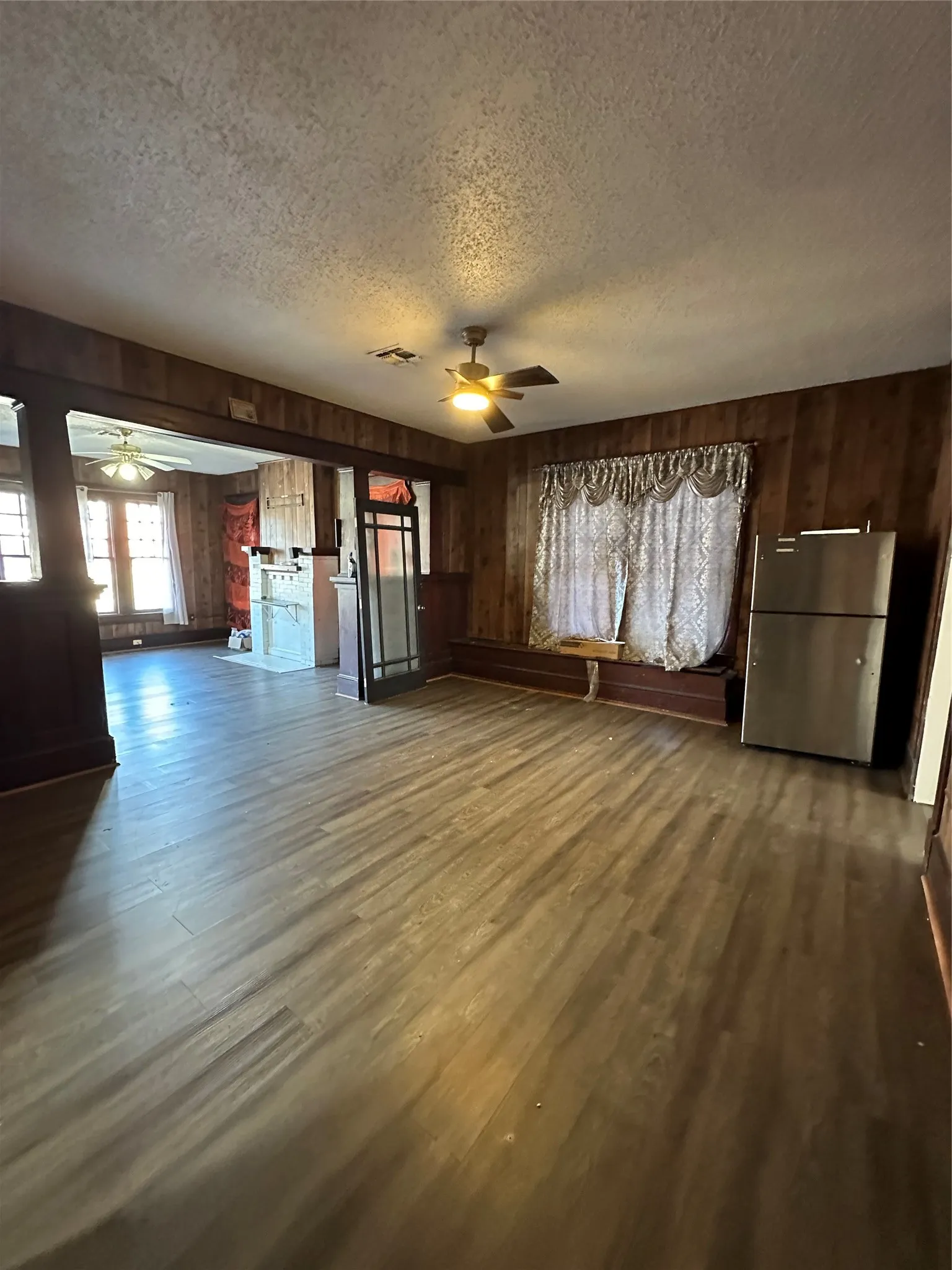 Unfurnished living room featuring a ceiling fan, wooden walls, dark wood finished floors, and a textured ceiling
