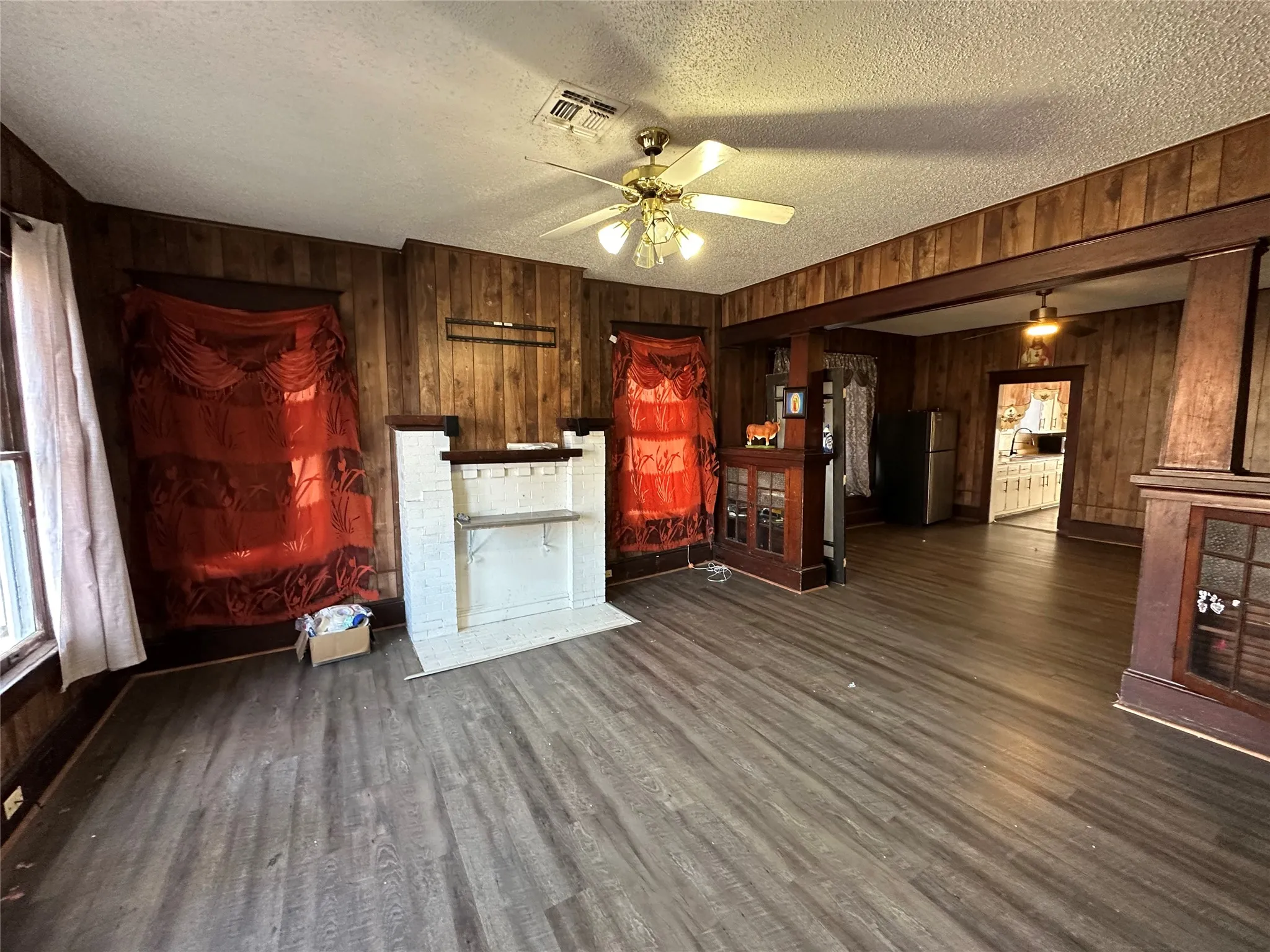 Unfurnished living room featuring wood walls, ceiling fan, a textured ceiling, and dark wood-style floors