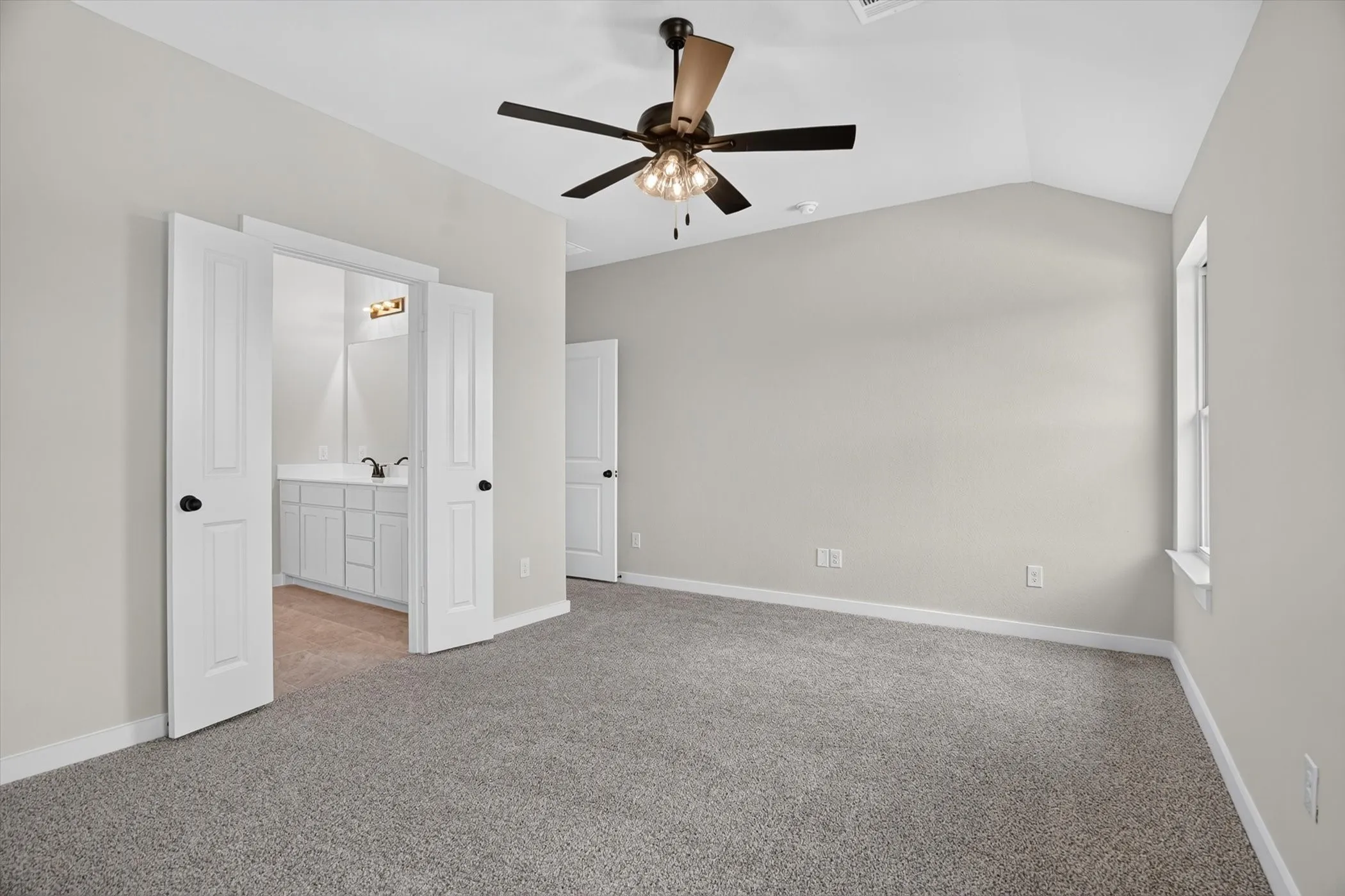 Vaulted ceiling with a ceiling fan, light gray wall paint, carpeted flooring, and a window with a white frame