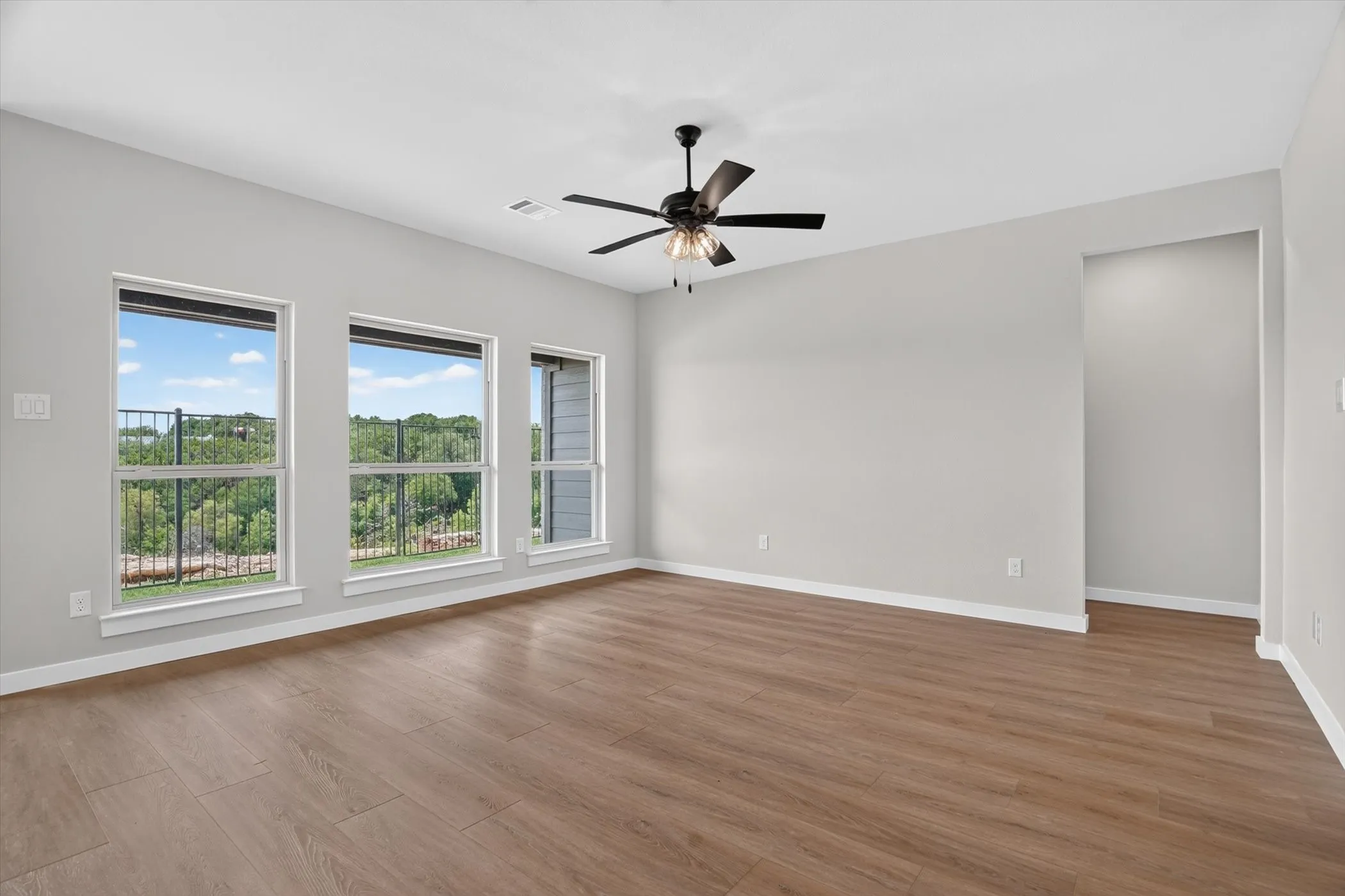 Wood-finish flooring, multiple windows, contemporary ceiling fan, recessed niche, light-toned walls