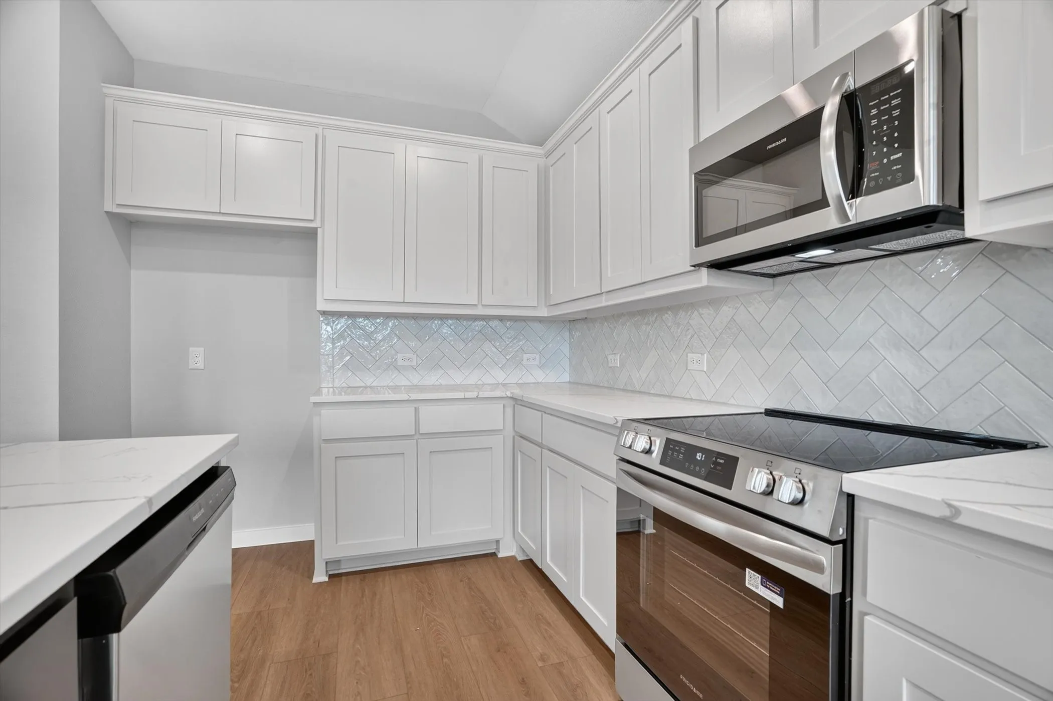 White shaker-style cabinetry, light wood-finish flooring, white countertops, and a herringbone pattern tile backsplash