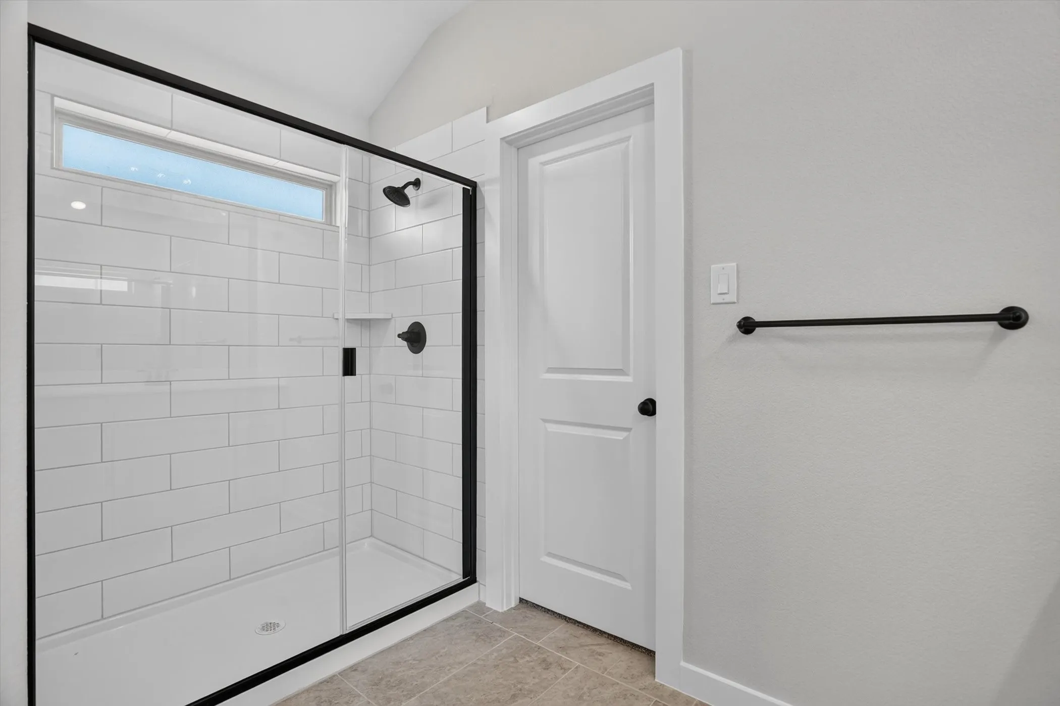 Glass-enclosed shower with subway tile surround, matte black fixtures, and a transom window