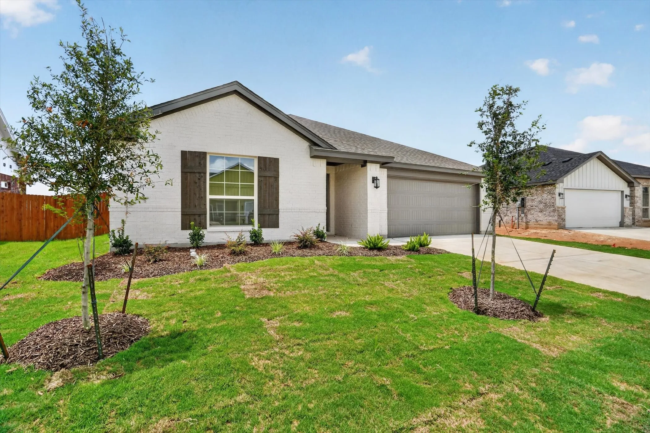White brick exterior with dark wood-finish shutters, a two-car garage, and established landscaping