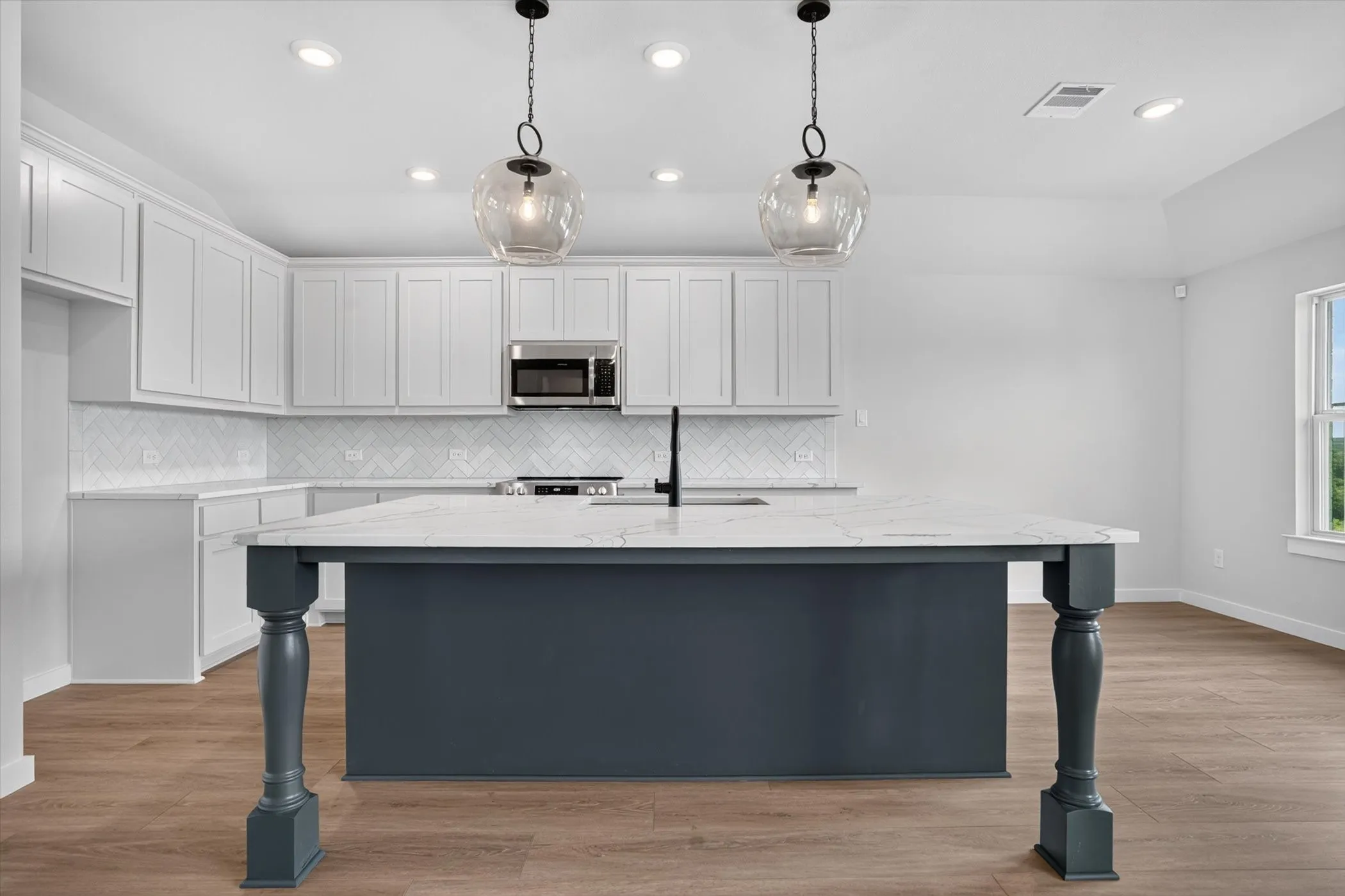 Kitchen featuring an expansive island with a solid surface countertop, pendant lighting, shaker-style cabinetry, and a subway tile backsplash