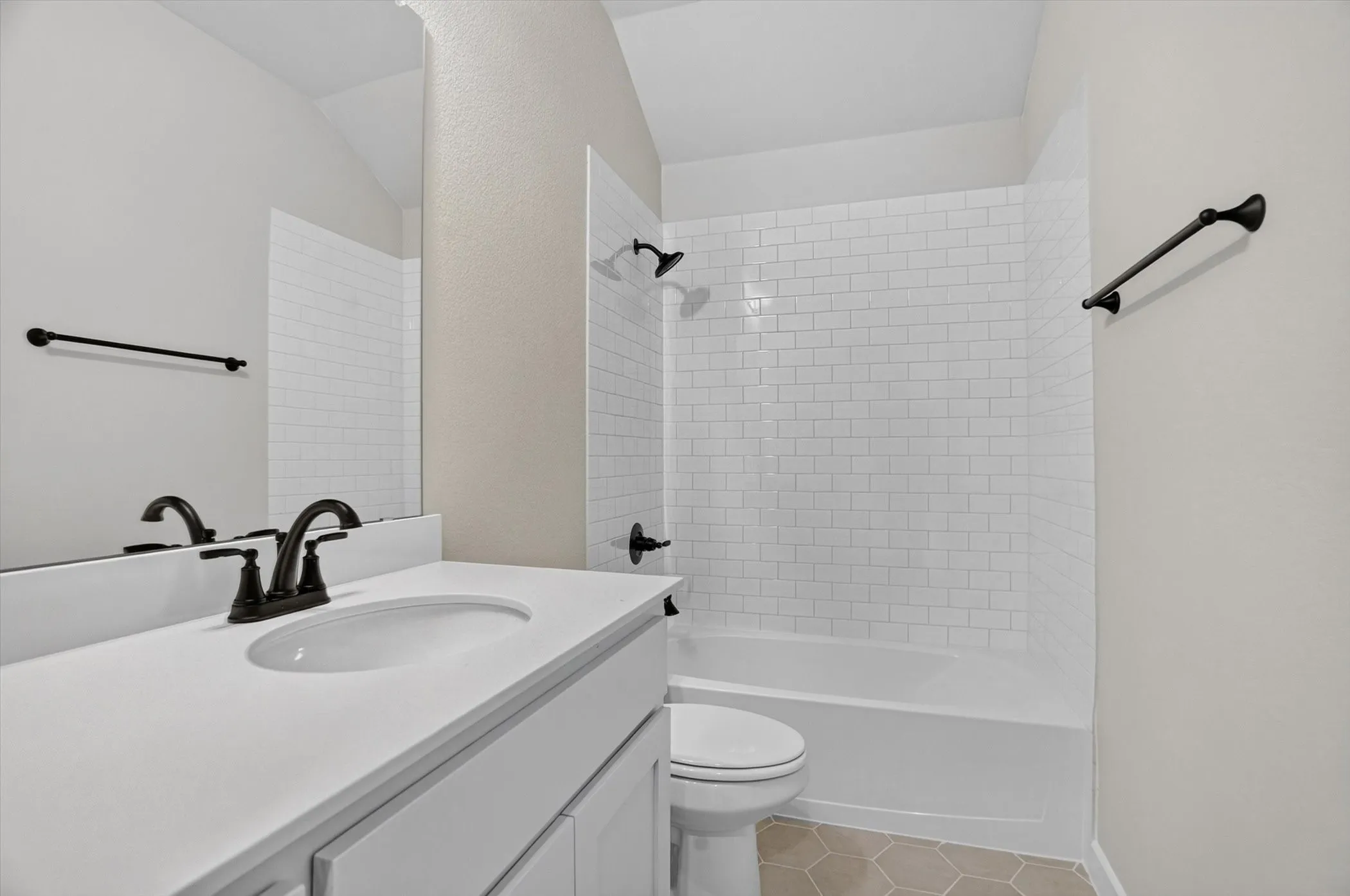 White subway tile shower surround, matte black fixtures, white vanity with integrated sink, and hexagon tile flooring