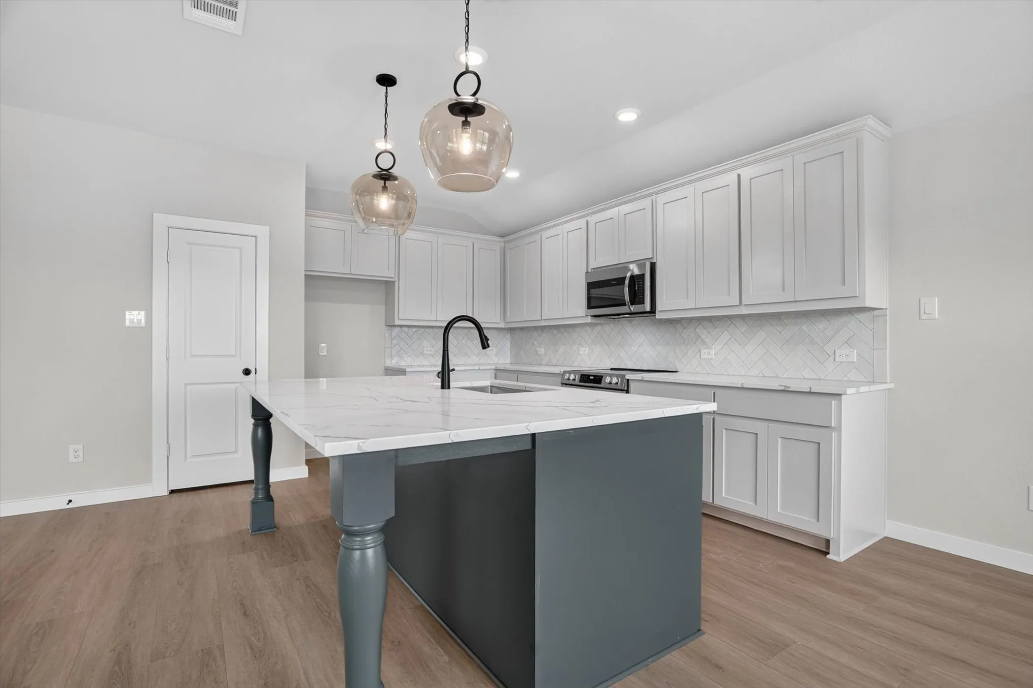 Kitchen island with a light-toned countertop, wood-finish flooring, white cabinetry, dark-finish appliances, and pendant lighting