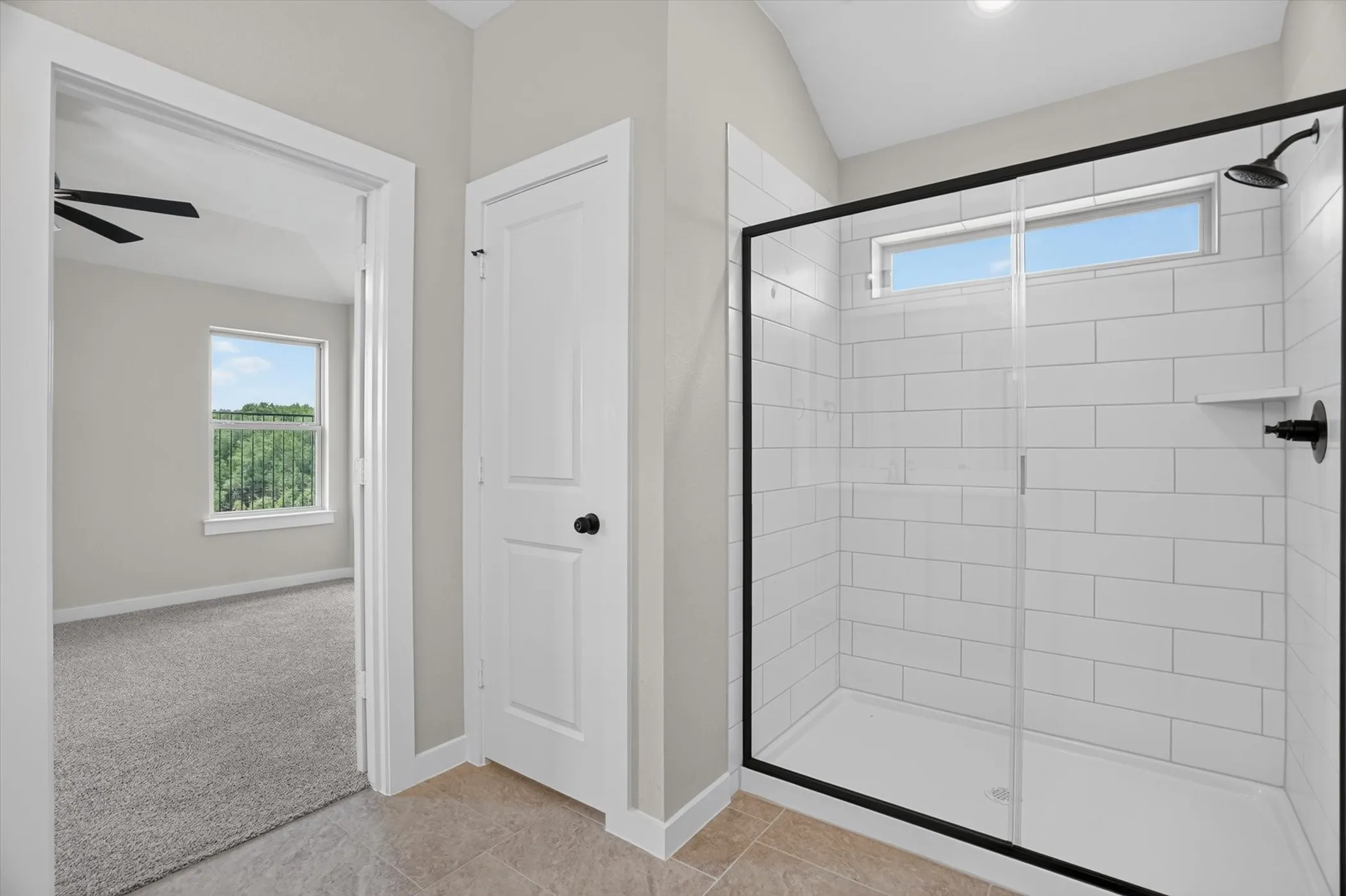 Walk-in shower with black-framed glass enclosure, white subway tile surround, and transom window