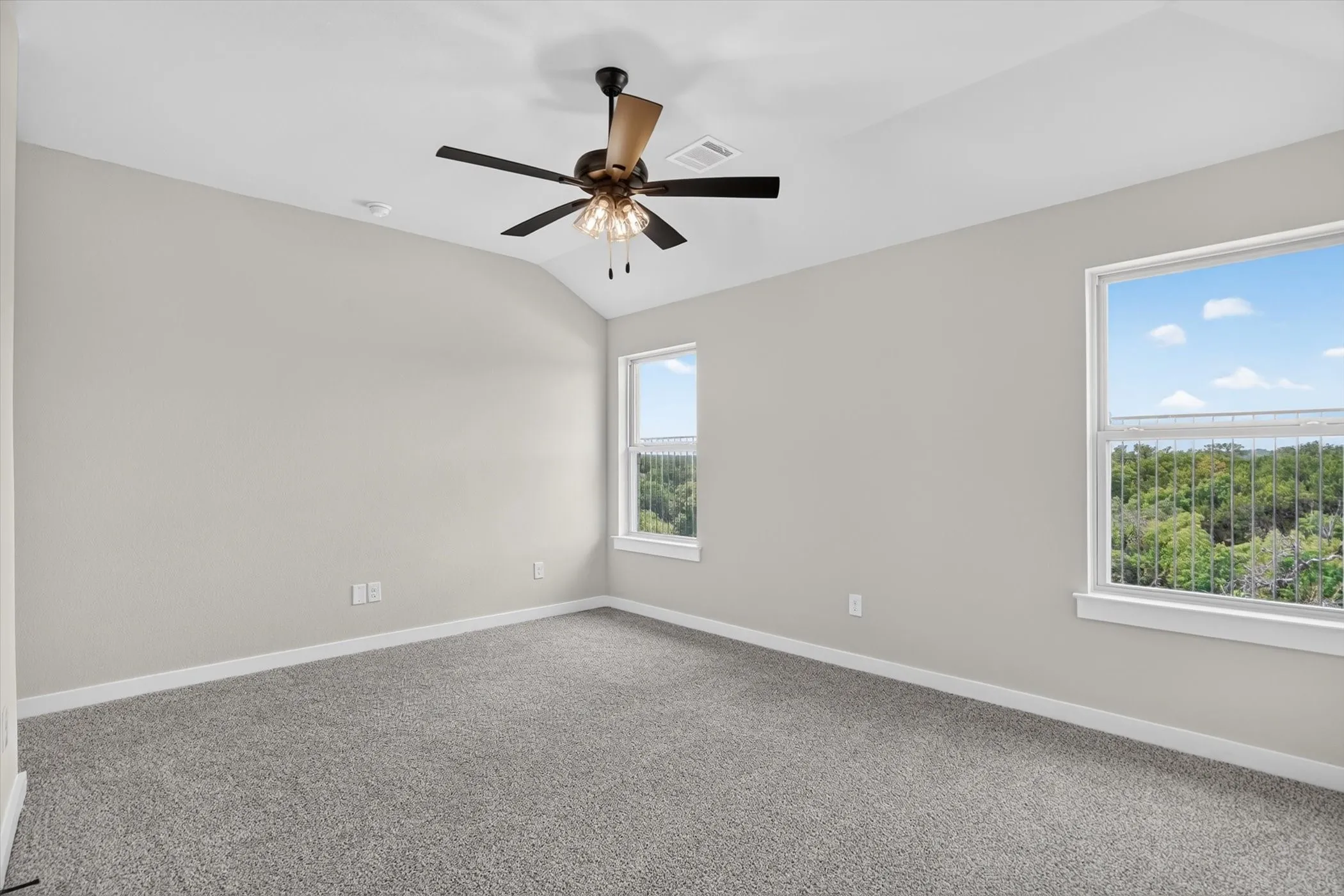 Vaulted ceiling with an integrated ceiling fan and light fixture, neutral carpet flooring, and two windows