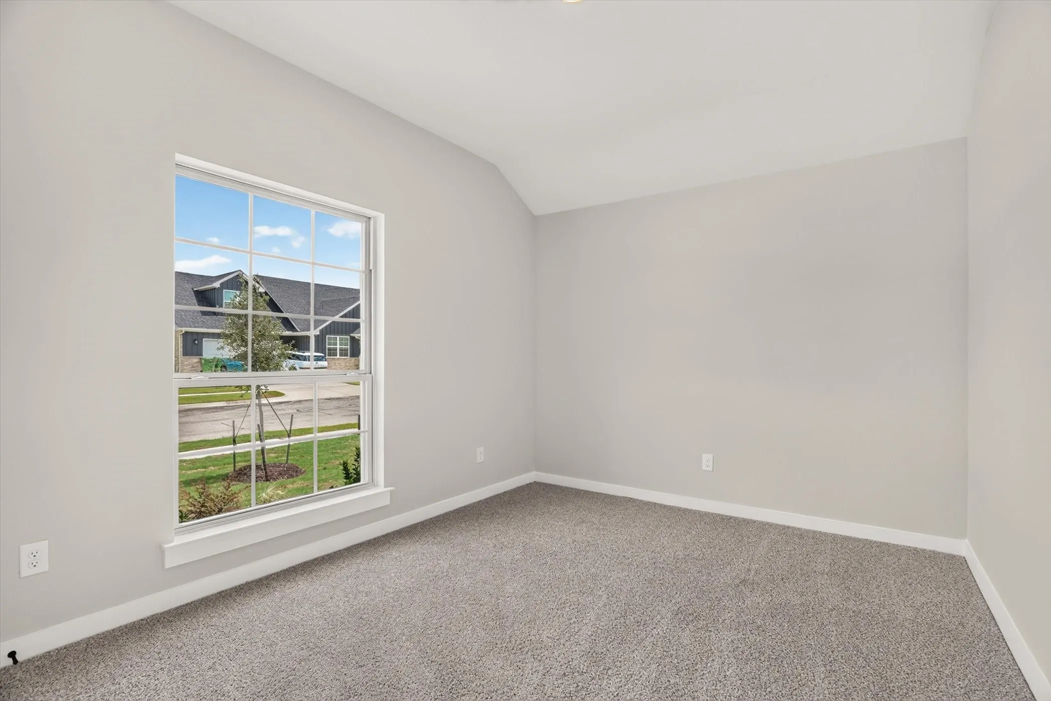 Neutral tone painted walls, textured carpeting, vaulted ceiling, and a large window with white trim