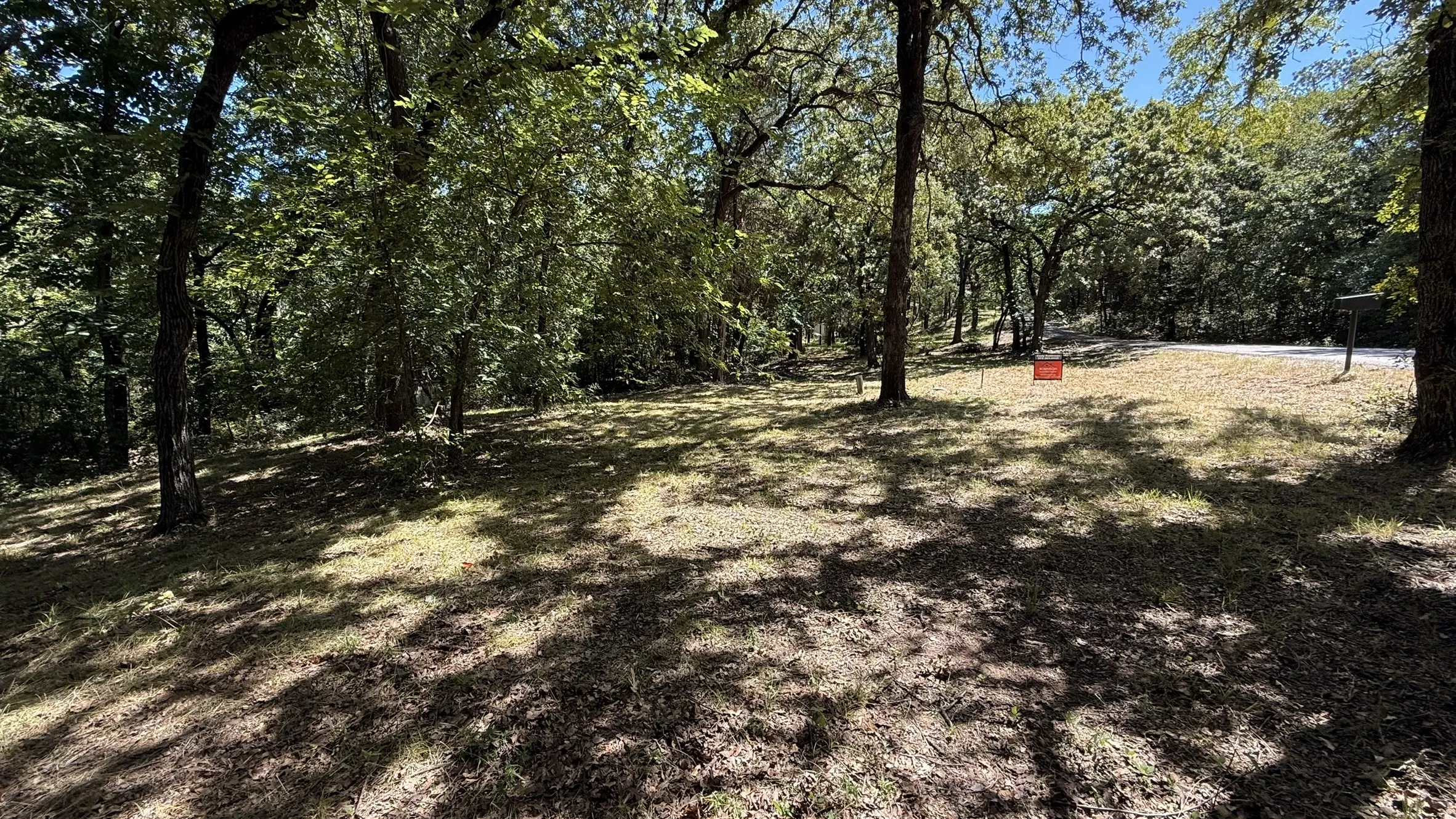 Wooded lot featuring a mix of mature trees and open grassy areas
