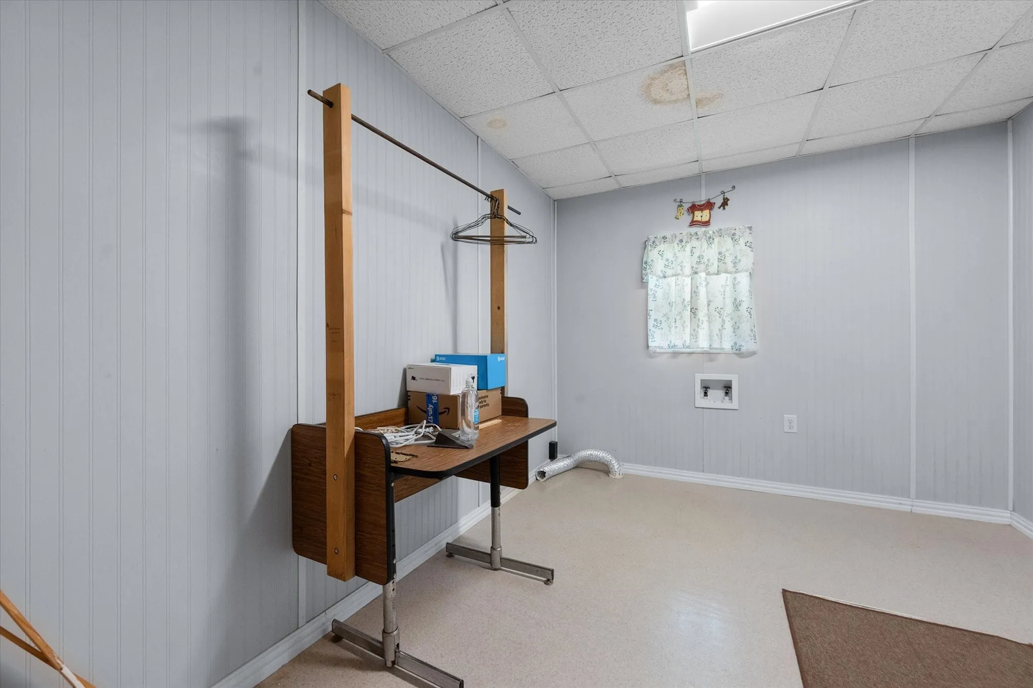 Utility room featuring paneling walls, a drop ceiling, and a window with a valance