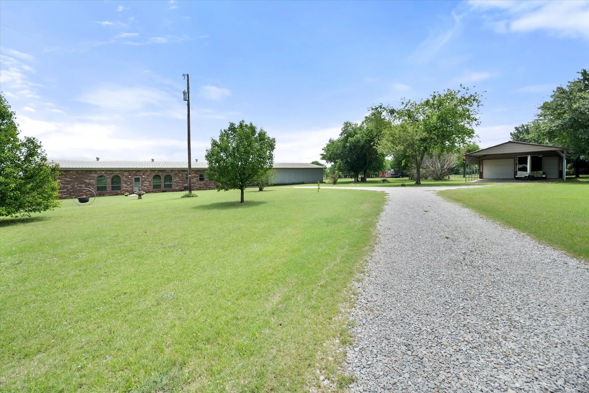Expansive gravel driveway leading to a brick-front structure with arched windows, surrounded by green lawns and mature trees