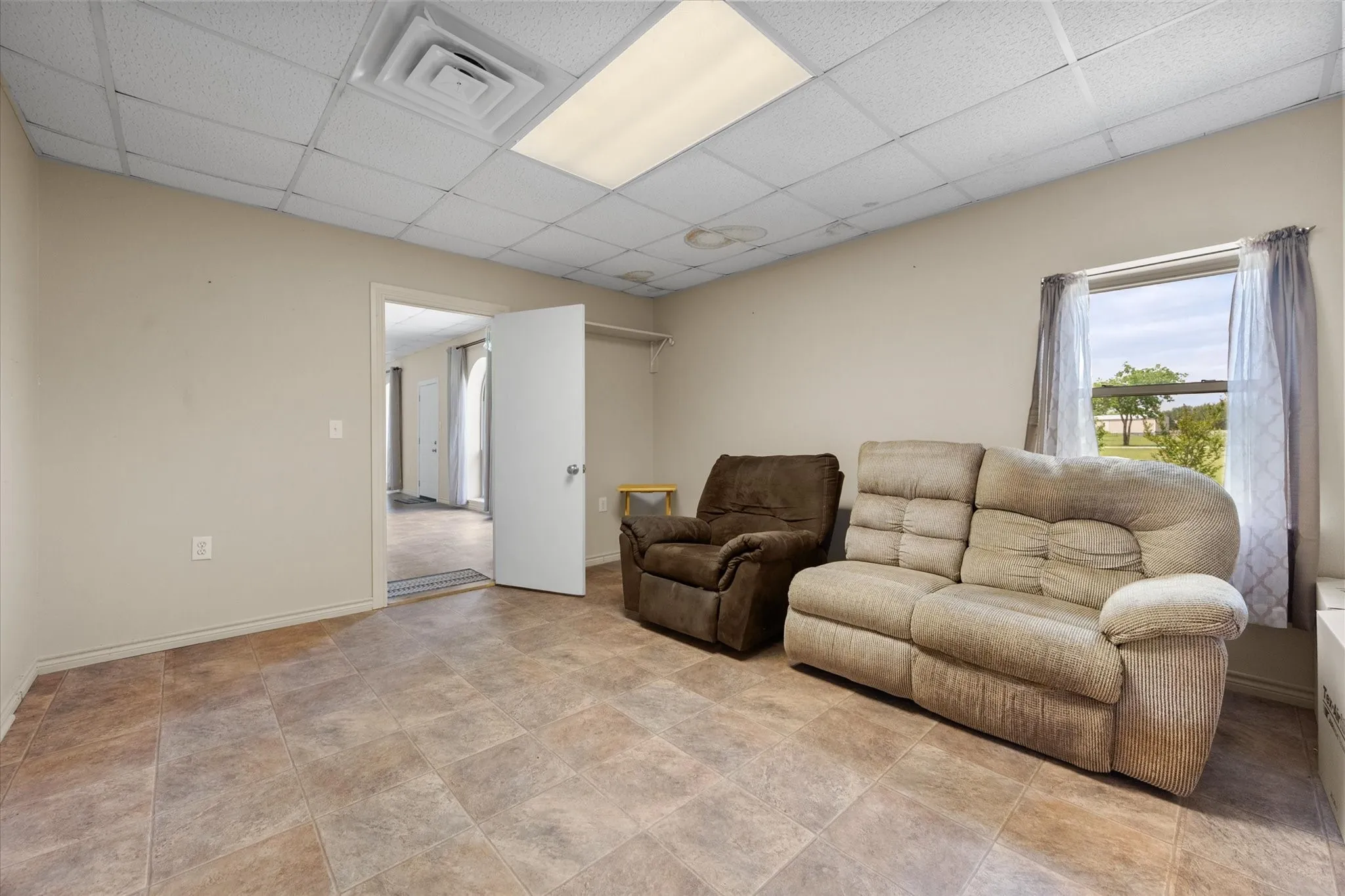 Interior room featuring neutral wall paint, tiled flooring, a drop ceiling with recessed lighting, and a window with natural light