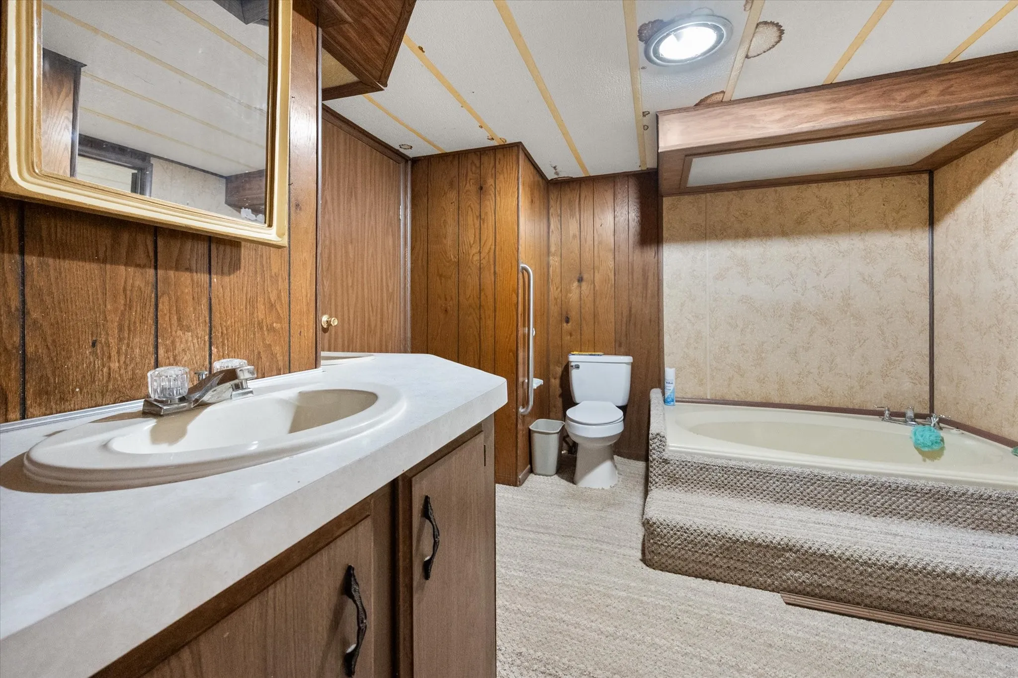 Bathroom featuring a built-in vanity with an integrated sink, wood-paneled walls, and a recessed bathtub with a textured surround