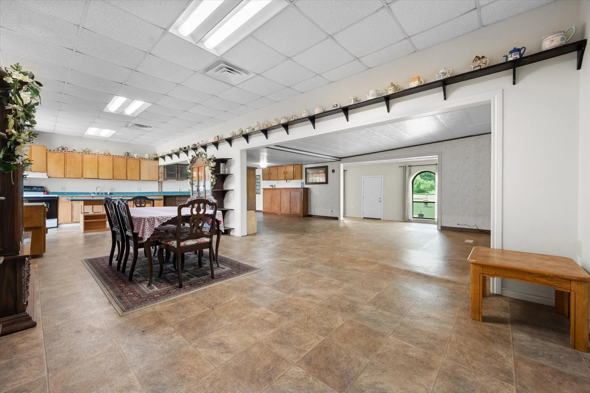 Spacious kitchen and dining area featuring tile flooring, light wood cabinetry, recessed lighting, and an arched window providing natural light