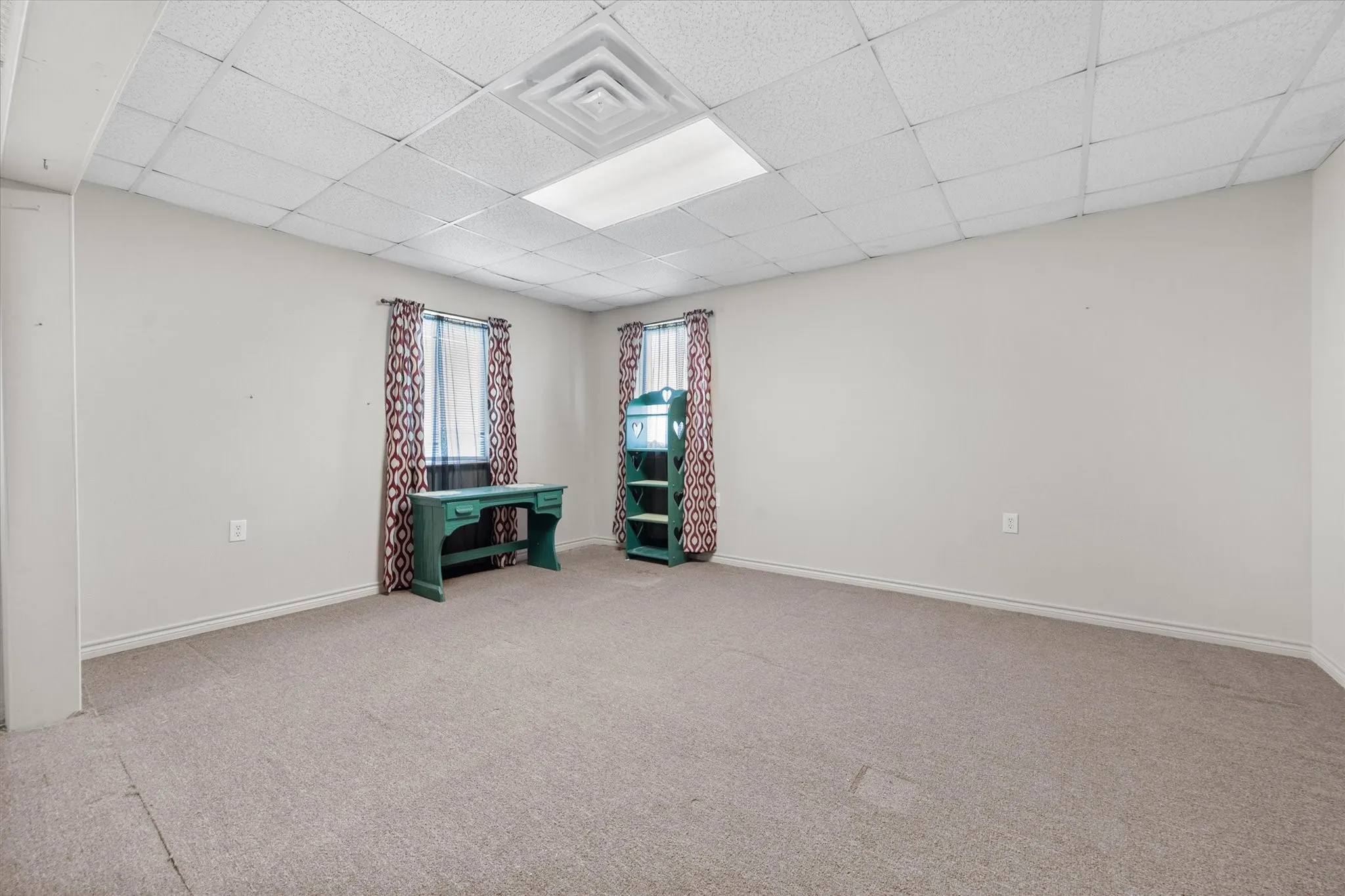 Spacious room featuring neutral carpeting, light gray walls, and a drop-ceiling with integrated lighting