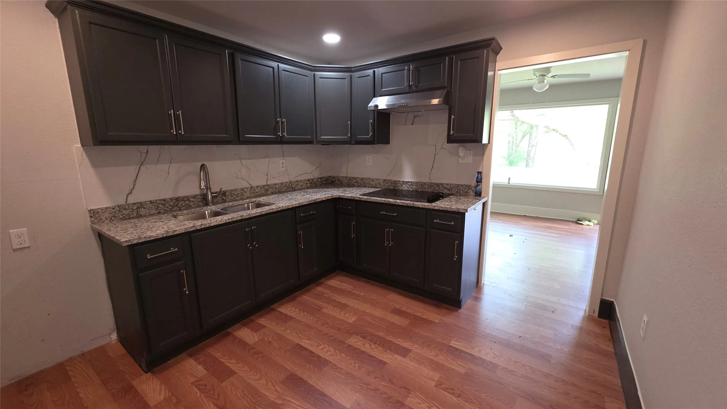 Kitchen with light stone countertops, light wood-type flooring, tasteful backsplash, and black electric stovetop