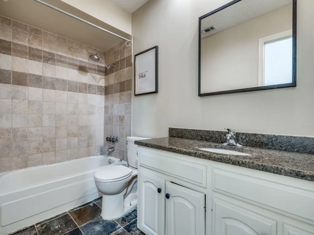 Full bathroom with toilet, tiled shower / bath combo, vanity, and a textured ceiling