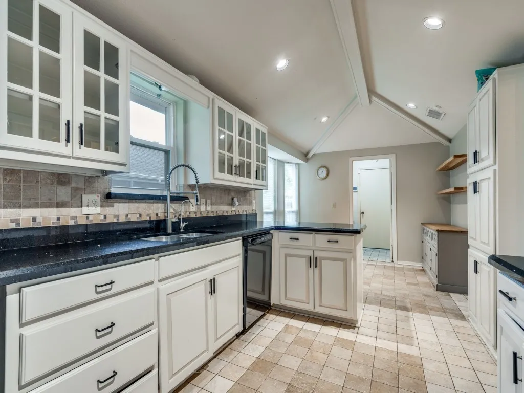 Kitchen featuring tasteful backsplash, vaulted ceiling with beams, white cabinetry, black dishwasher, and sink