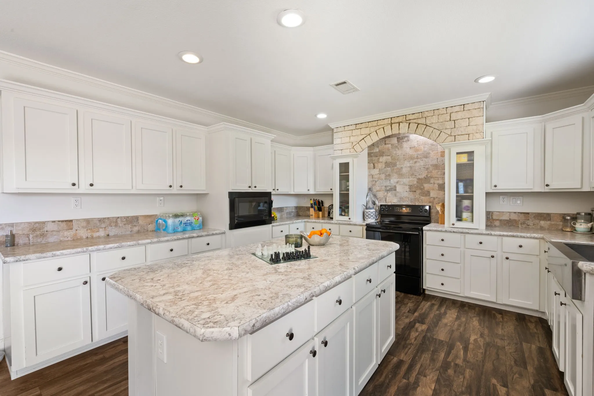 Kitchen with black appliances, crown molding, white cabinets, dark wood-style flooring, and a kitchen island