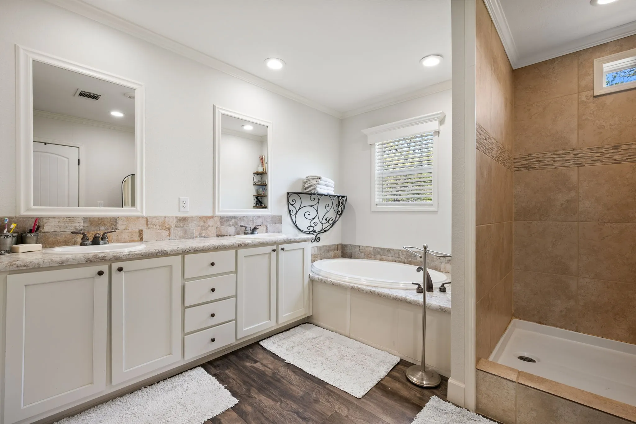 Bathroom with double vanity, a garden tub, crown molding, dark wood finished floors, and a tile shower